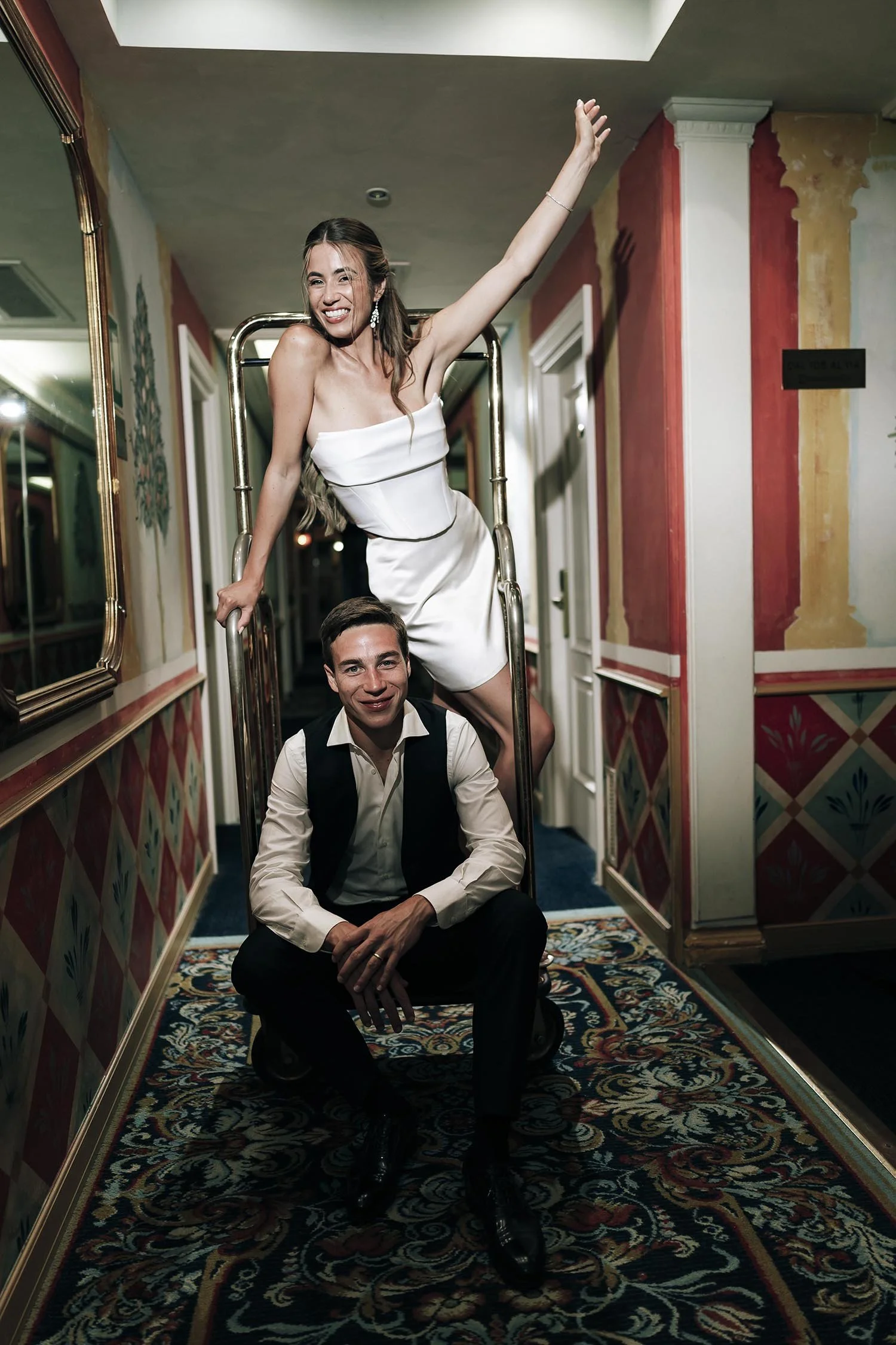 bride and groom sitting on a luggage cart along the hotel corridor at Monastero Santa Margherita in Todi