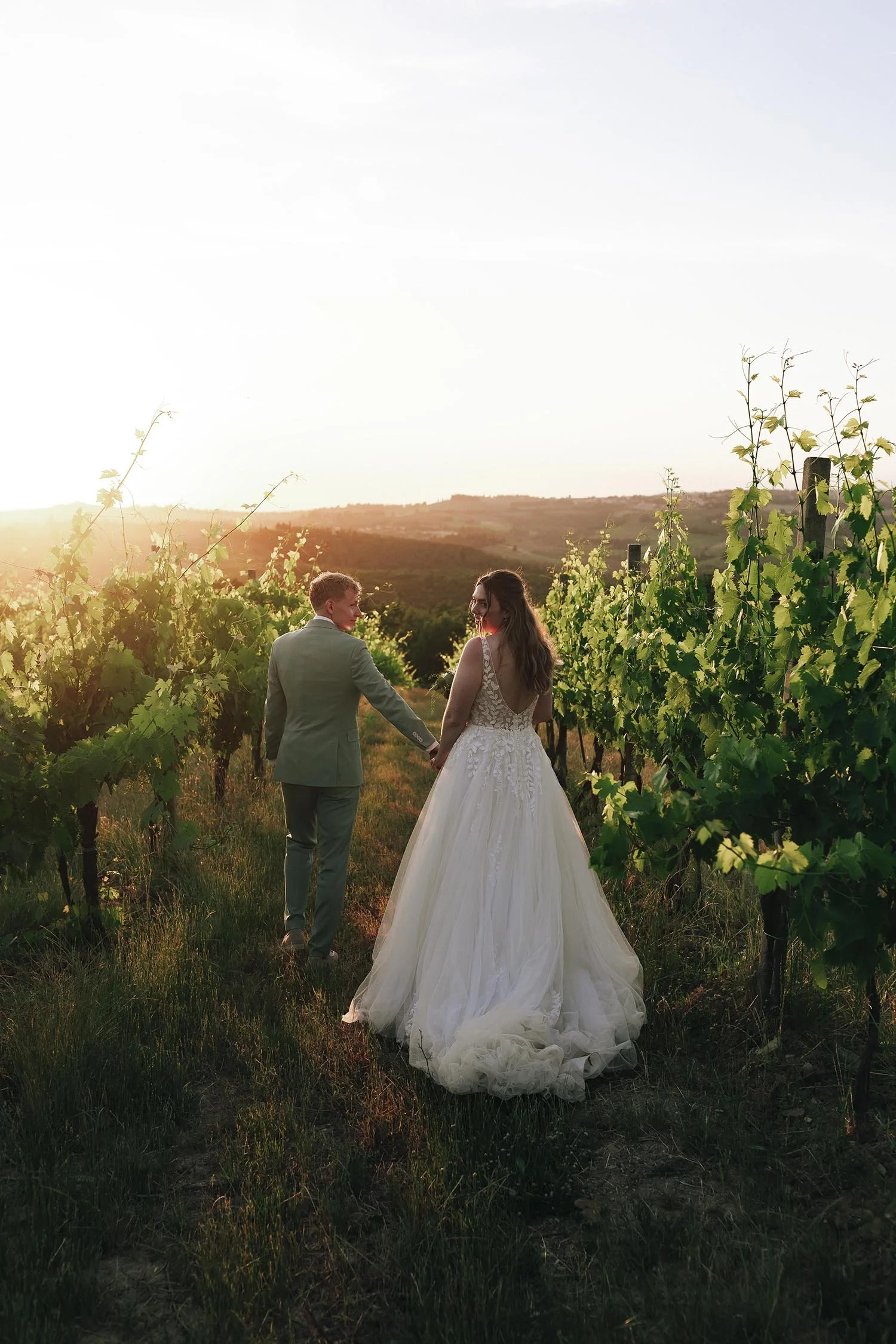 Bride and groom walking together in the viewyards with the sun setting behind the valley at Quercia al Poggio