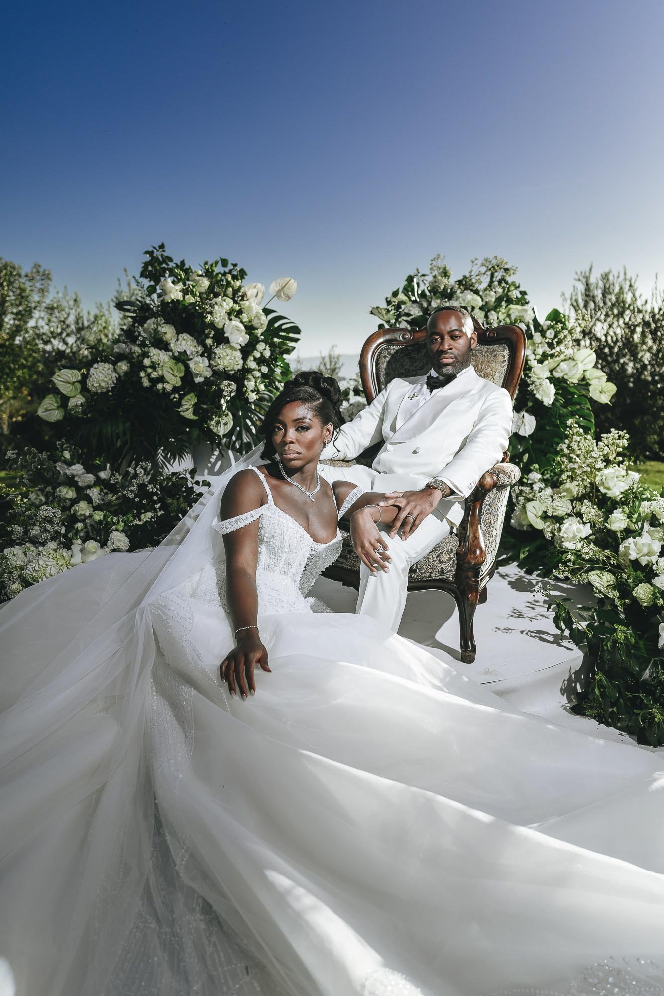 Bride and groom sit together posing for the camera with flowers in the background