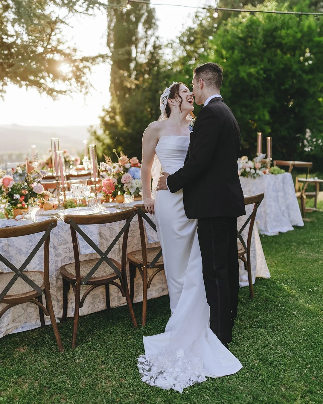 Groom and bride kiss each other by the dinner tables with the sun setting