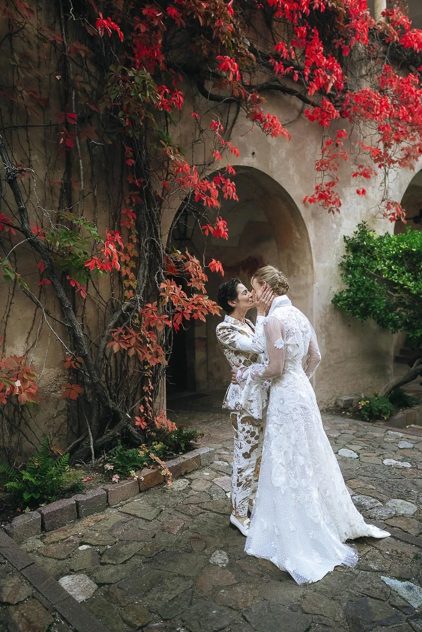 Two brides kissing each other under red autumn leaves in the courtyard of Schloss Freudenstein