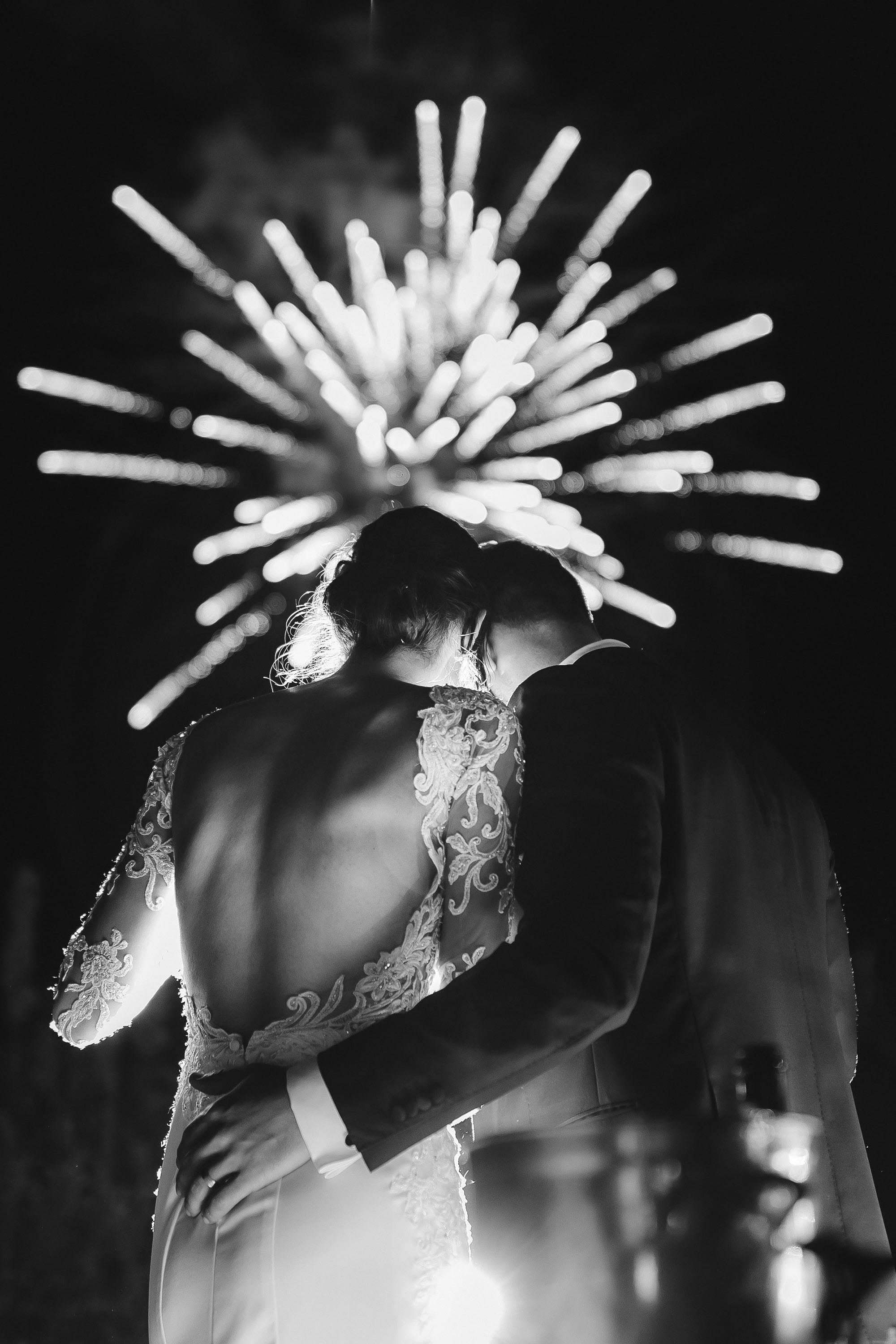 bride and groom holding each other watching the fireworks by night