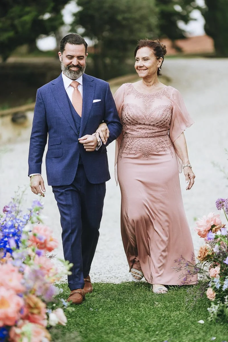 The moments of the ceremony at Terre di Nano wedding venue in Tuscany with the groom walking dowen the aisle weith his mother. Photo by Rellini art studio award winning married photographers duo