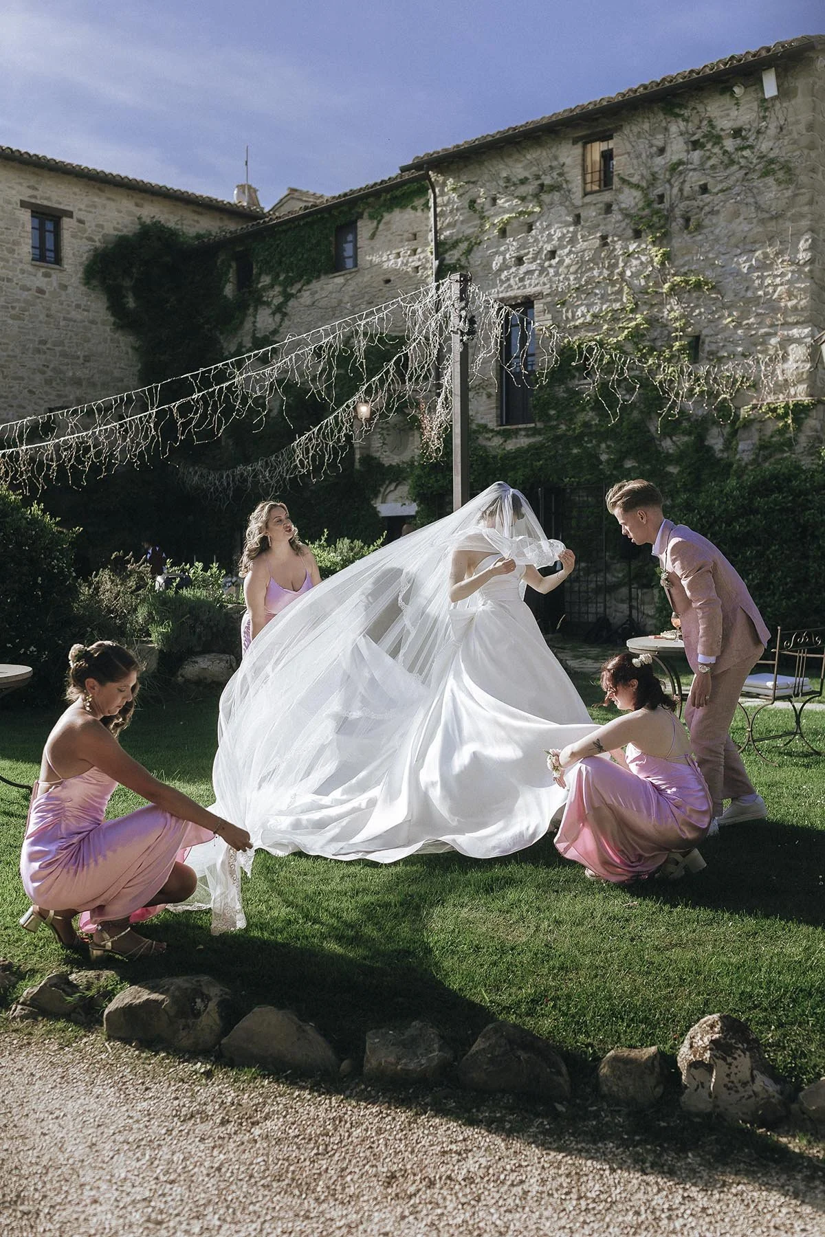 bridesmaids helping the bride fixing her veil in the courtyard of Castello di Petrata in Umbria