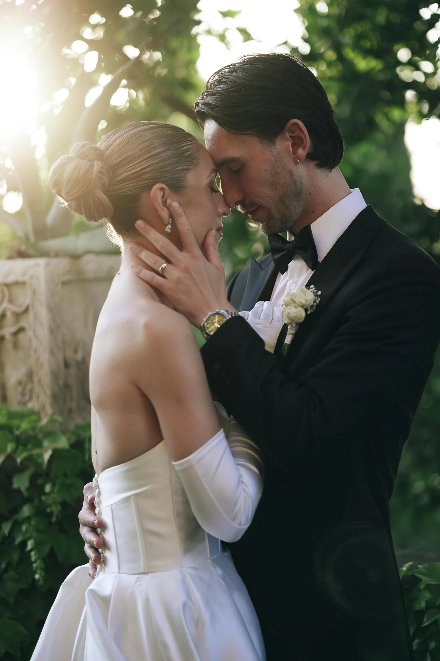 Bride and groom facing each other and kissing with a huge tree in the background