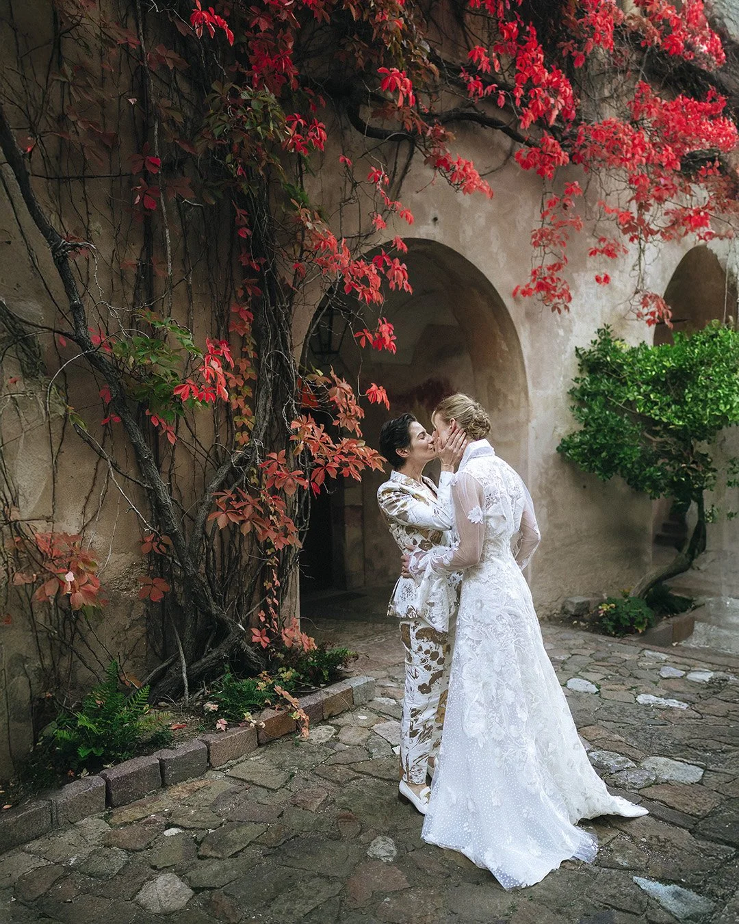 Two brides kiss each other with autumn leaves in a castle
