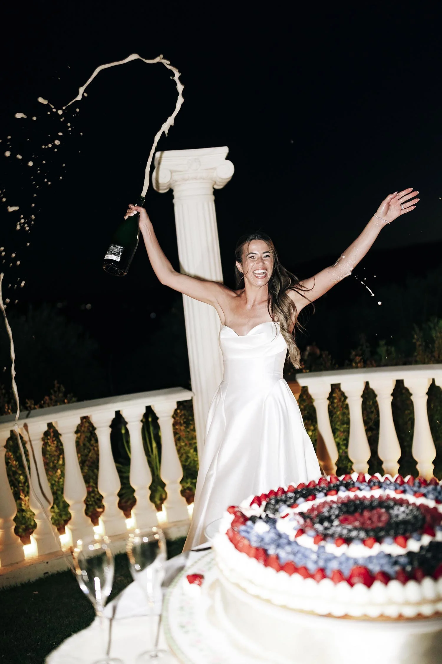 bride opening a bottle of champagne and celebrating after cutting the cake