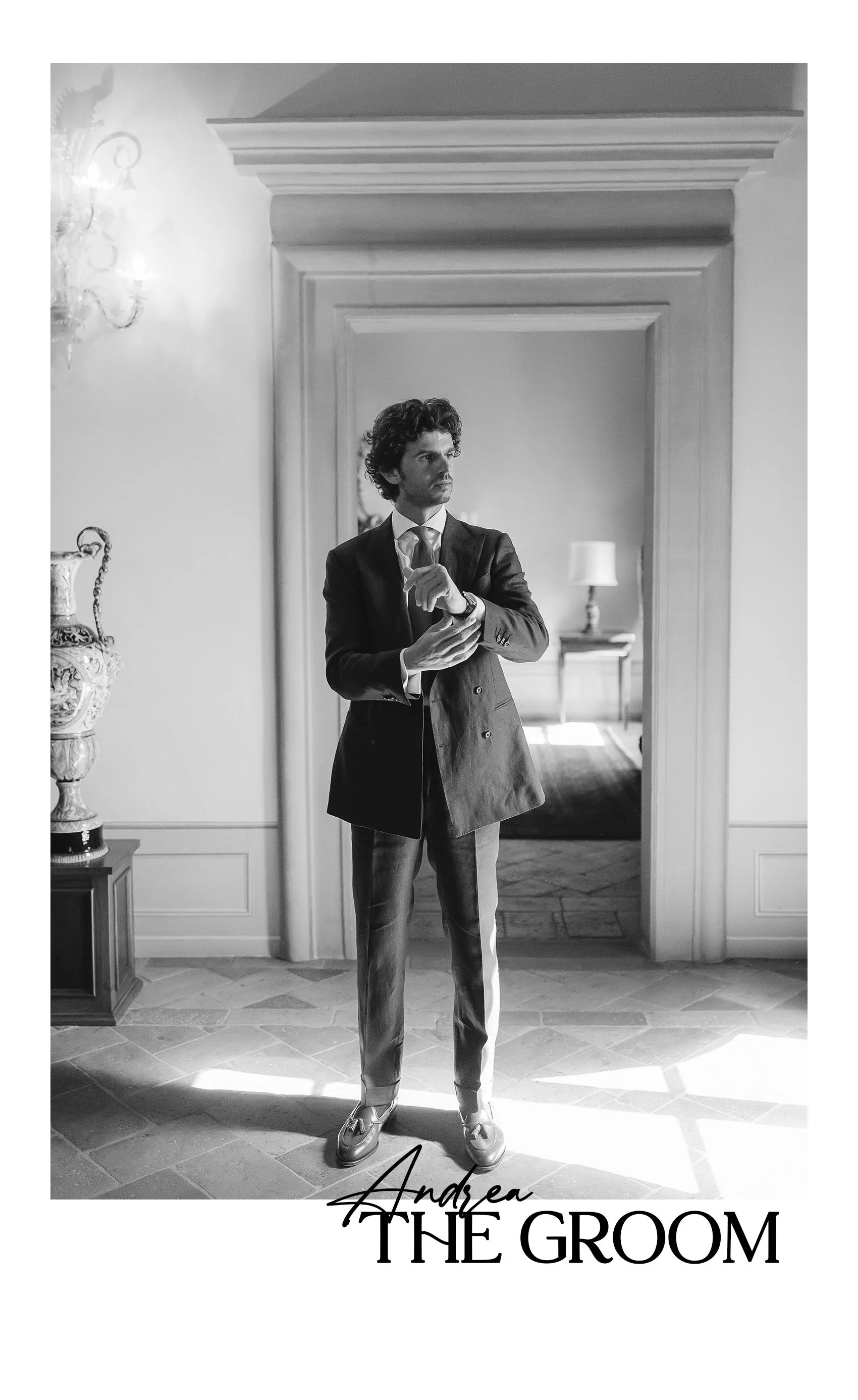 A black and white photograph of a young man dressed in a suit, adjusting his cufflink in front of a doorway in an elegant room with vintage decor. The image includes the text 'Andrea THE GROOM' at the bottom.