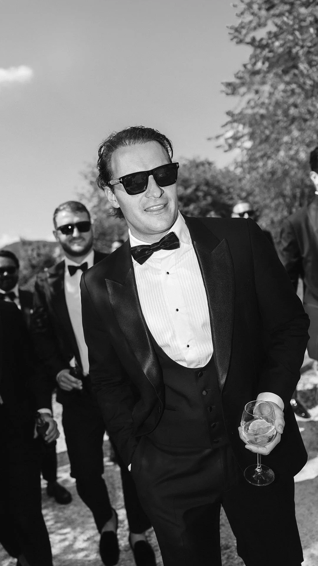 candid photo of the groom walking with his groomsmen holding a glass of wine