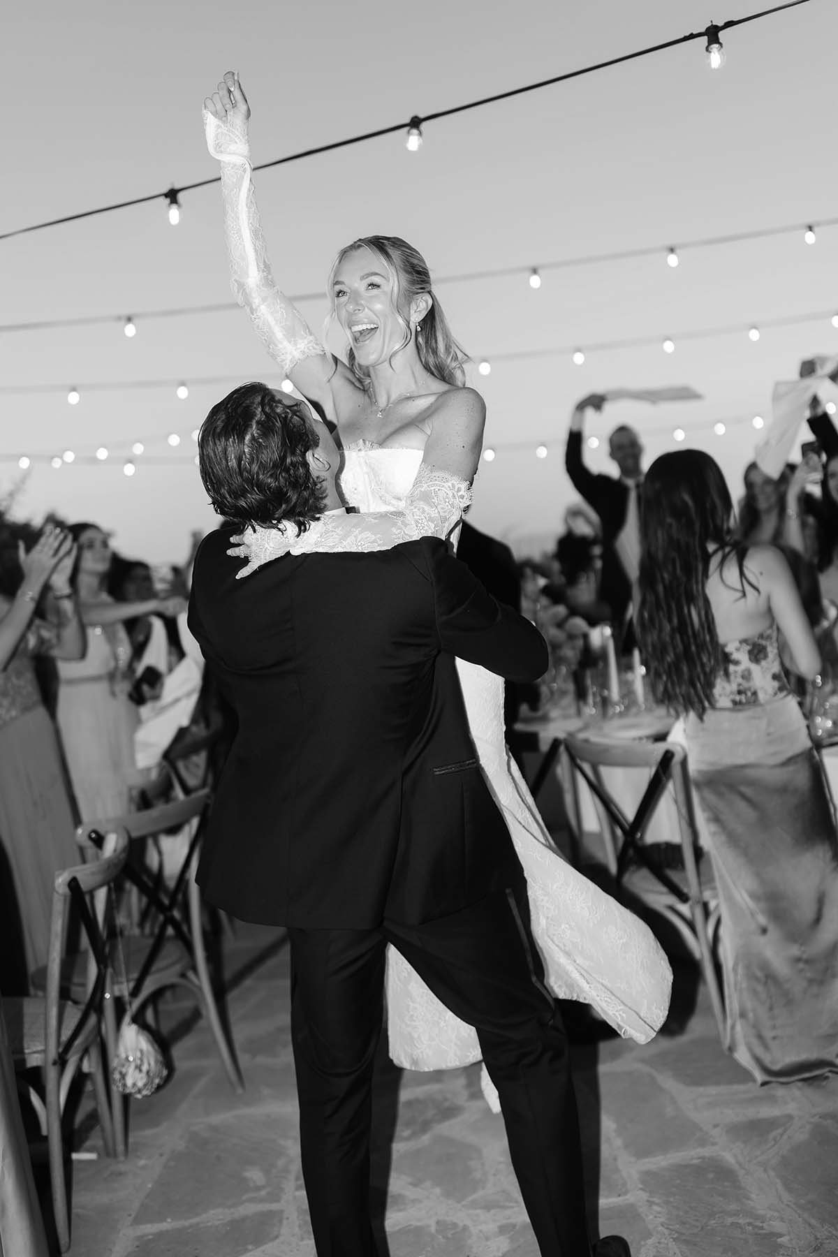 groom picking up the bride who celebrates with all the guests with napkins in their hands at the dinner tables at Castello di Petrata
