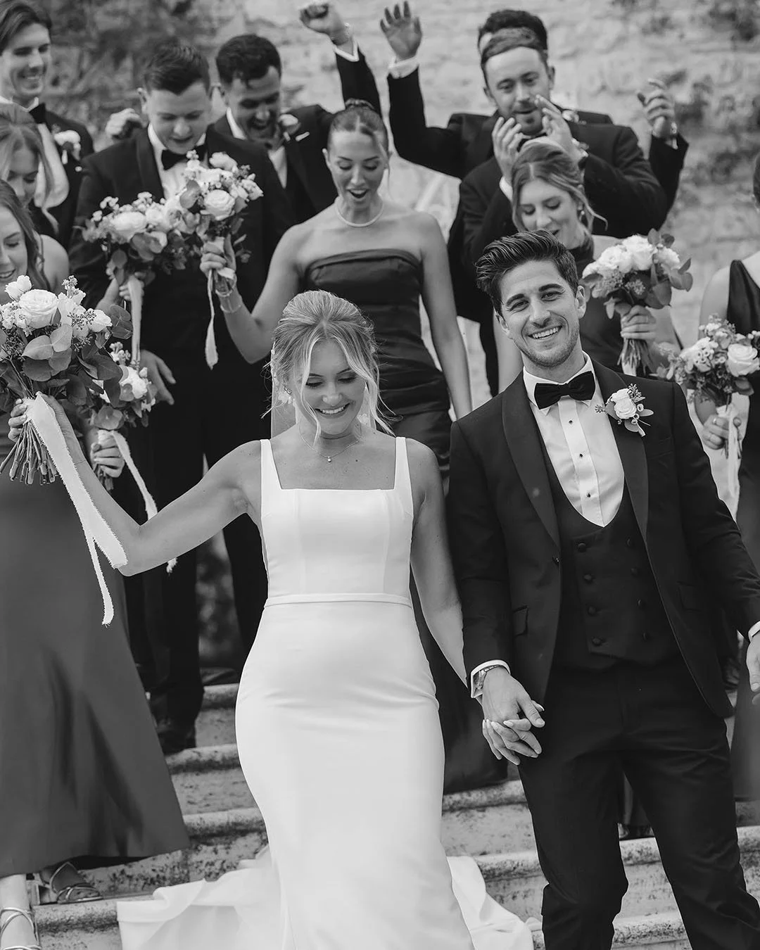 bride and groom walking down the stairs followed by their friends celebrating
