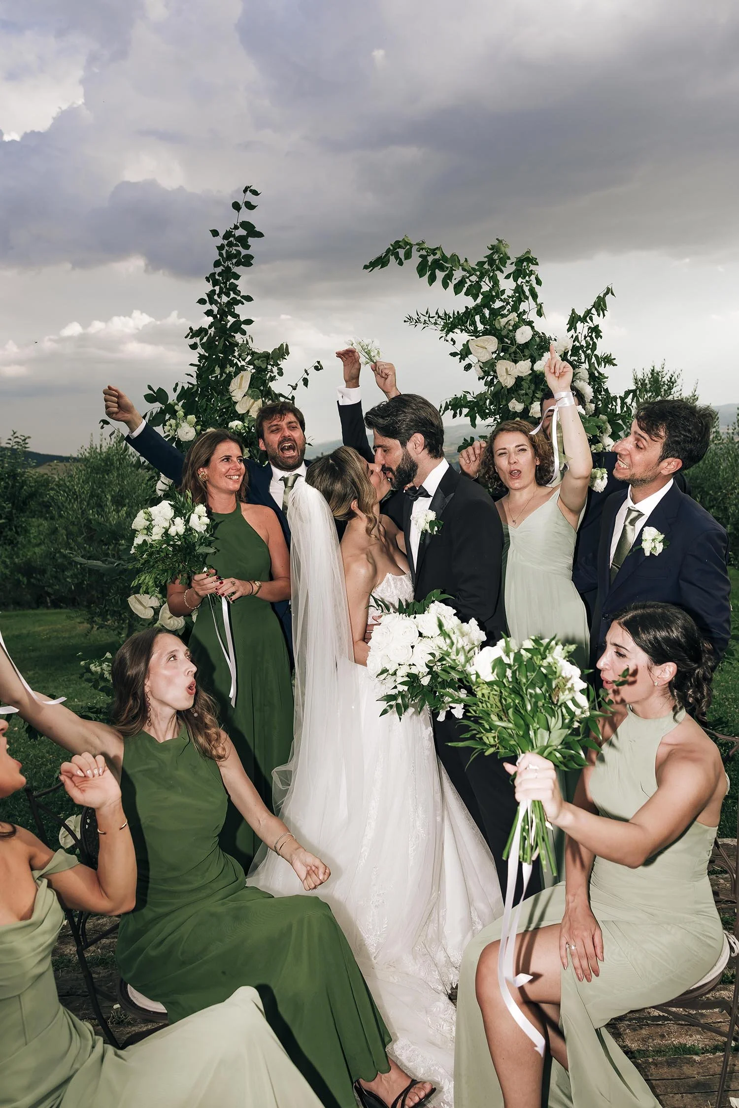 bride and groom kiss each other with their bridal party celebrating in the background