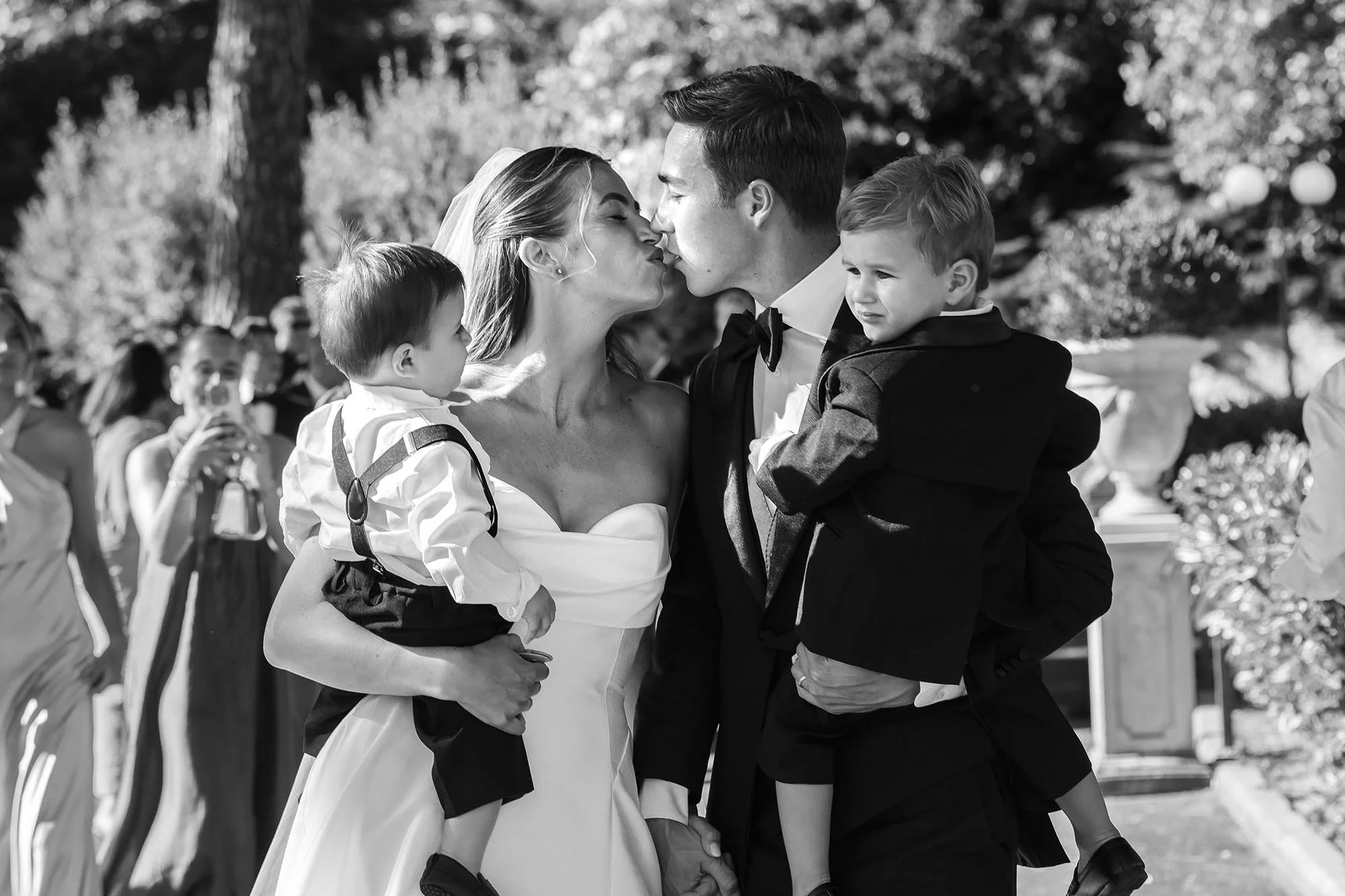 bride and groom walking away from the ceremony holding their two sons and kissing