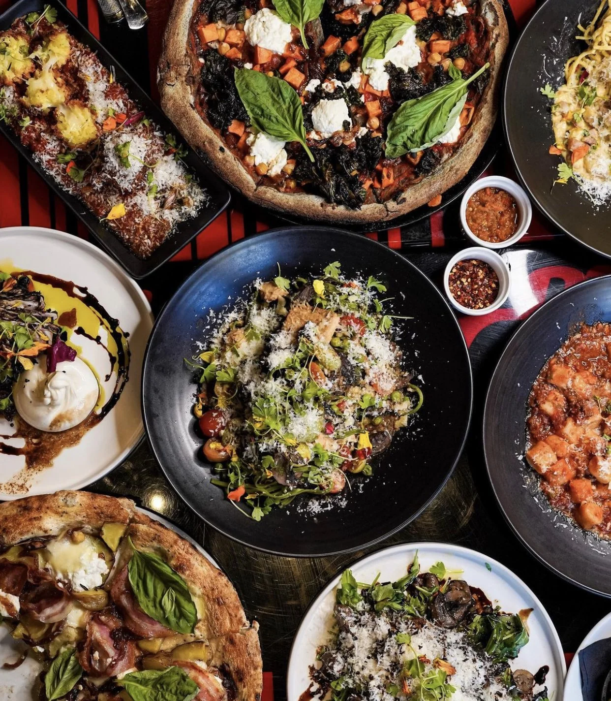 A variety of Italian dishes on a table, including pizza, pasta, and salads, with condiments and sauces.