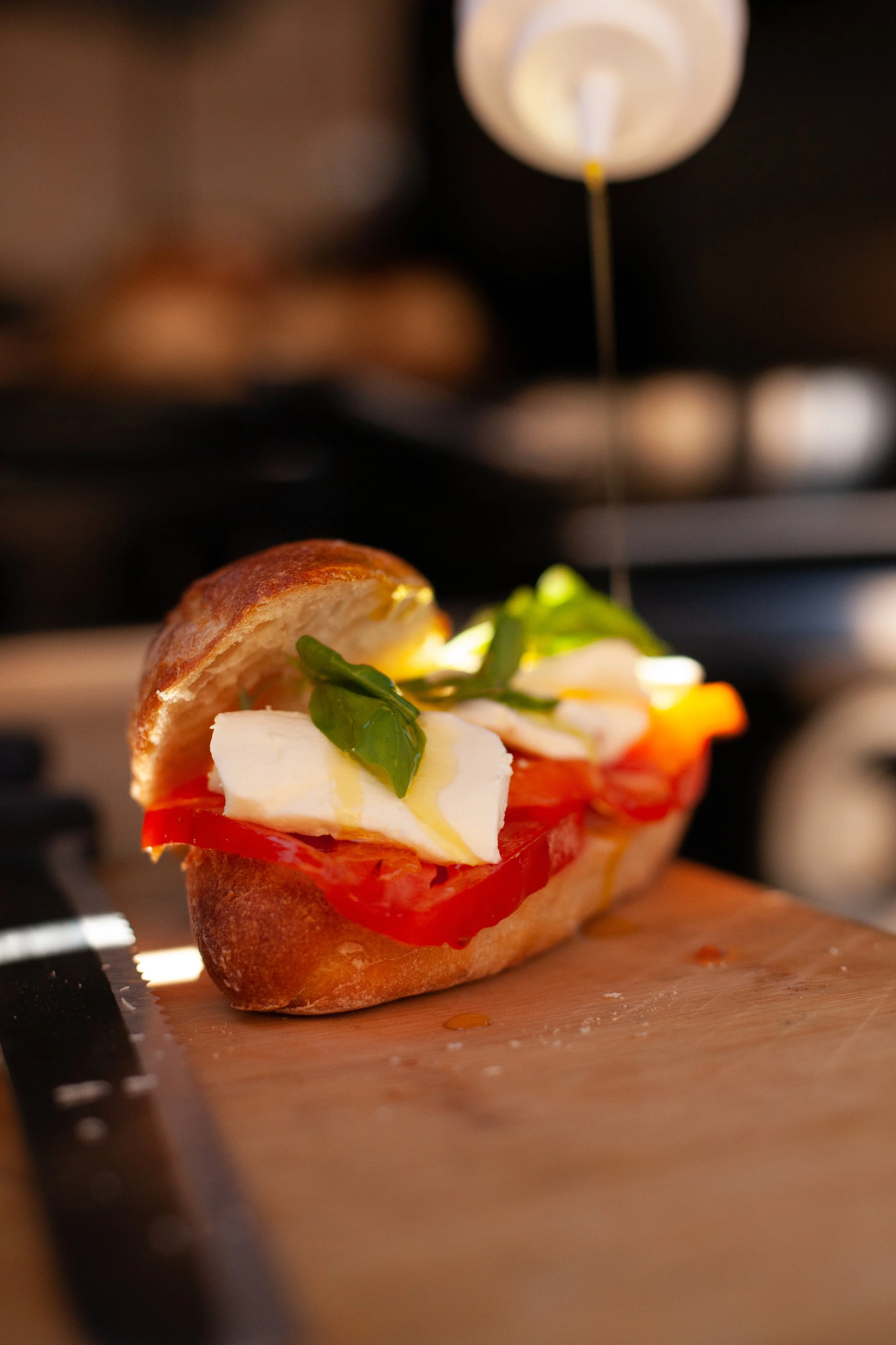 Open-faced sandwich with tomato, basil, mozzarella, and olive oil on a bread roll, on a wooden cutting board.
