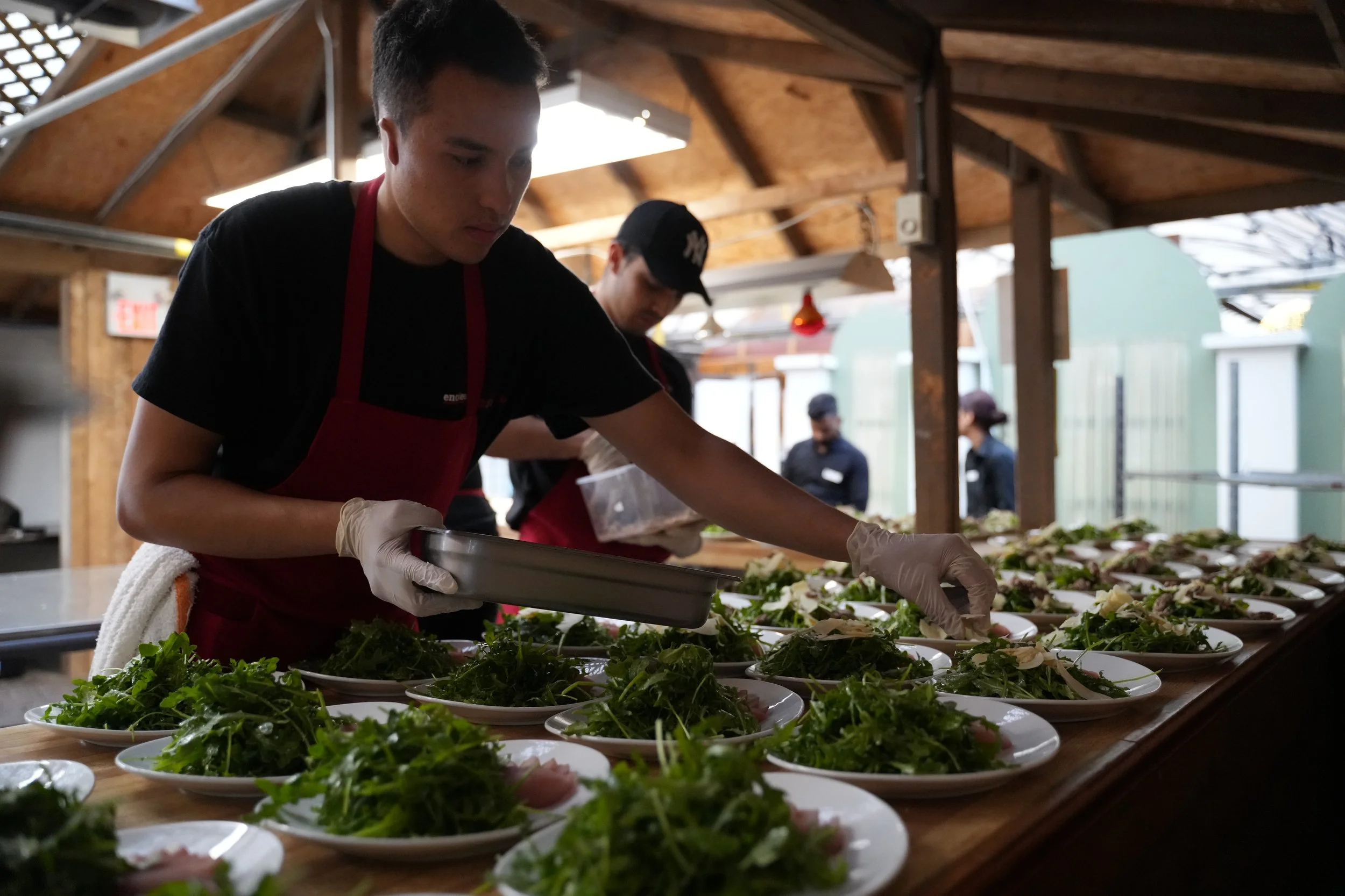 Chef preparing salads with greens and toppings on a wooden serving table at a restaurant.