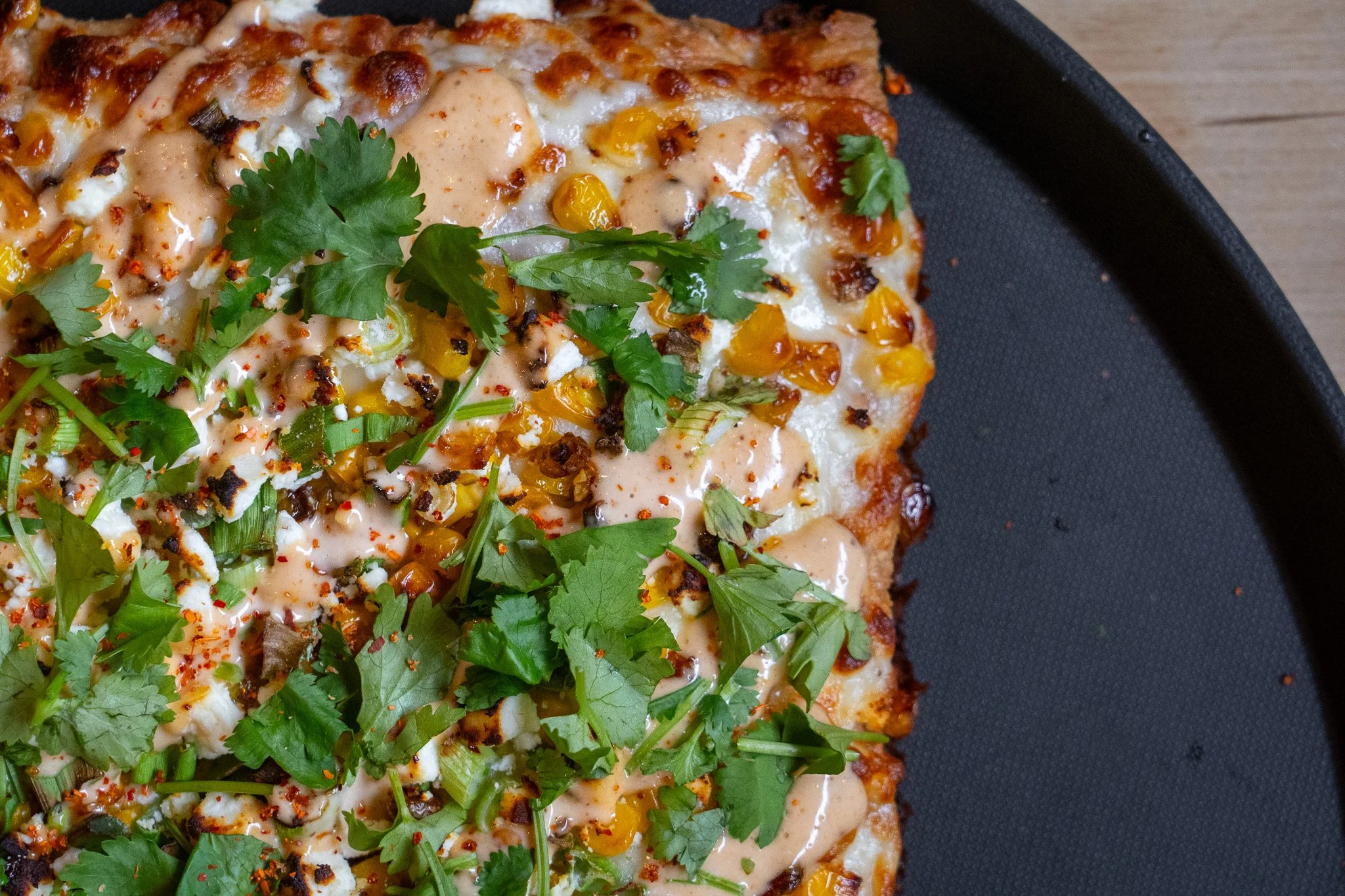 Elote: Garlic oil, mozzarella, charred corn, scallions, feta cheese, chipotle lime mayo drizzle, cilantro.