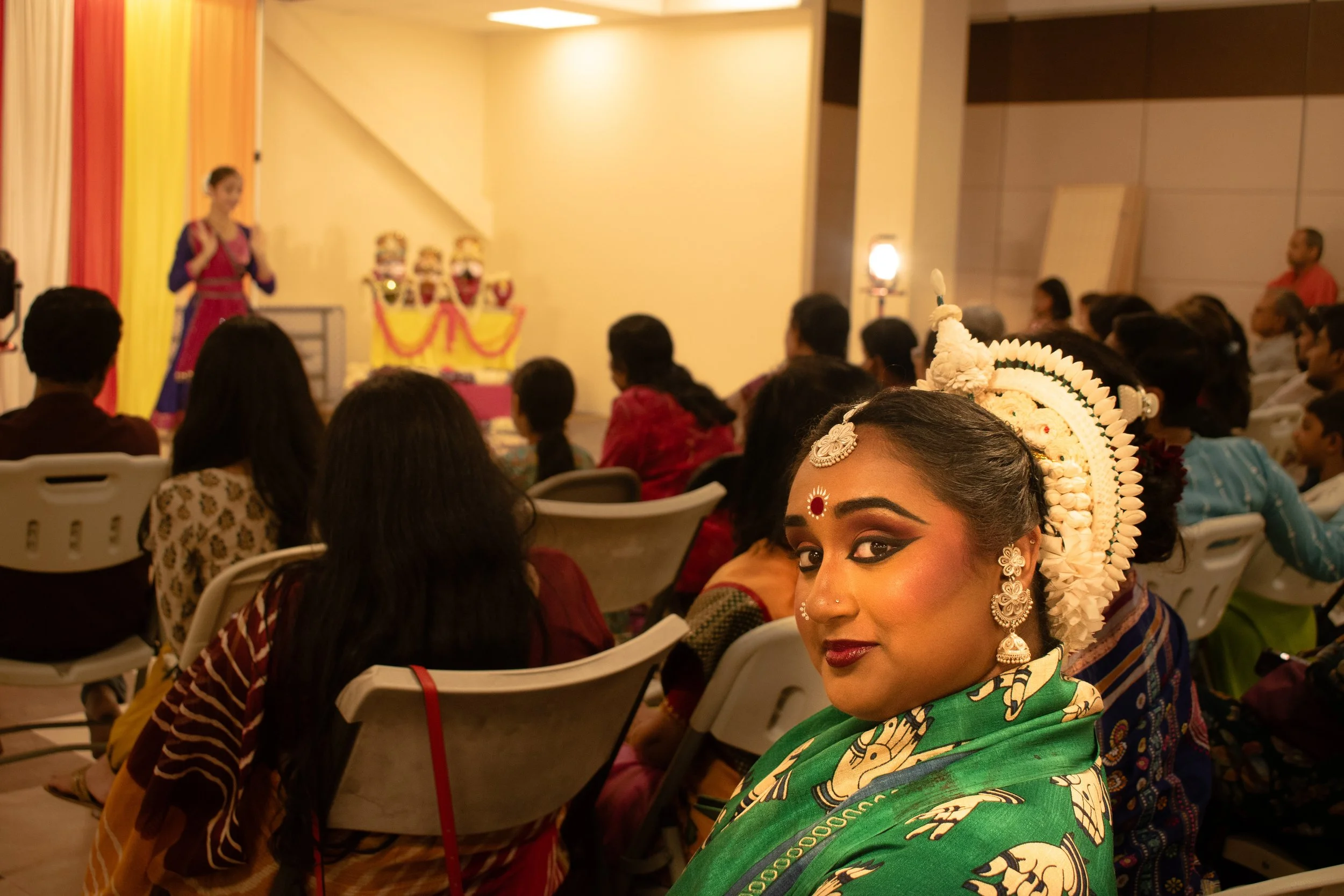 The lady here is dressed up in one of her traditional costumes and was performing Odissi dance, which is a type of Indian classical dance. She is wearing a bomkai saree. They're all waiting there for their turn to perform back to back showing differe