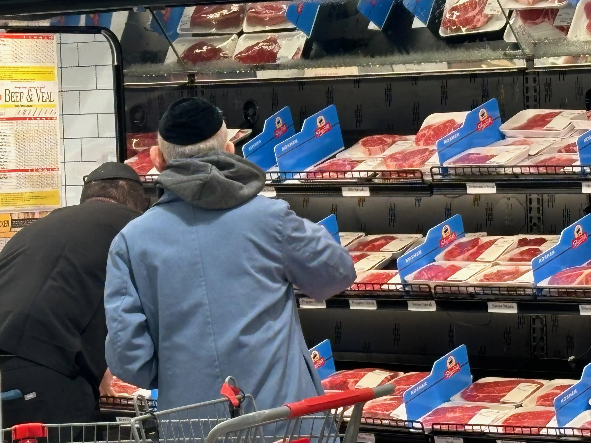 This is the kosher meat section and it's just kind of, I like the old guy and the young guy working together to stack the shelves.    

Orthodox Jewish men often wear yarmulkes, a brimless skull cap to show respect and humility to God and as a remind