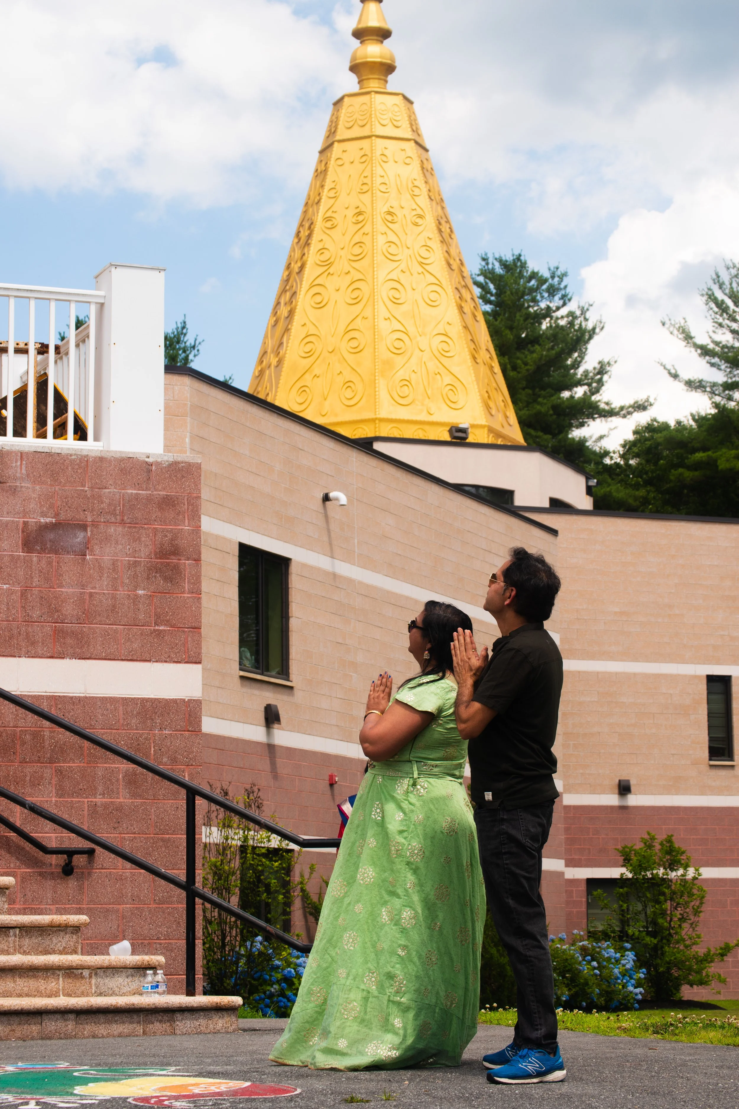 This is what an Indian temple looks like. Usually a dome, a pyramid shaped tower. The top of the tower is usually built with real gold. This couple is standing beside the temple and praying from outside by joining their hands and thanking the god. Ne