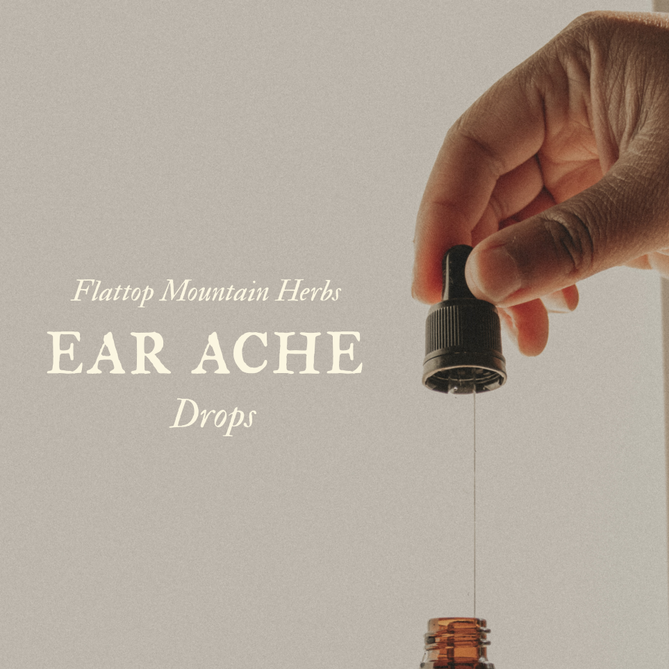 A hand holding a dropper above a small bottle, with a few drops falling into the bottle. The image features text about ear ache drops made from Flat-top Mountain herbs.