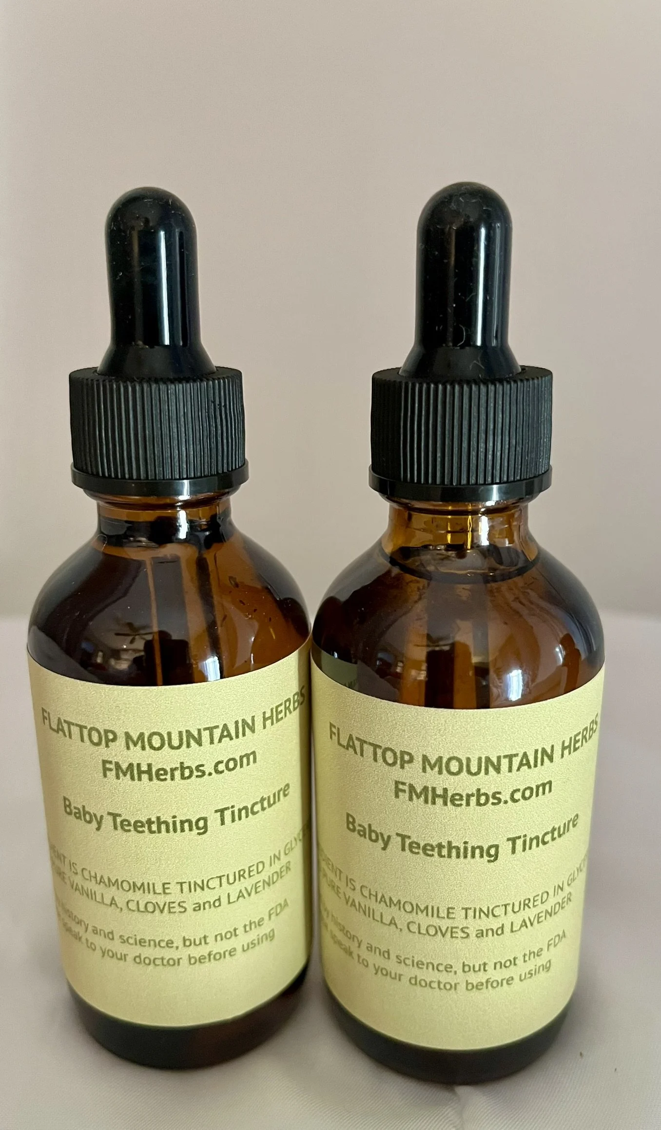 Two amber glass bottles of baby teething tincture with black dropper caps, labeled "Flattop Mountain Herbs" and website FMHerbs.com.