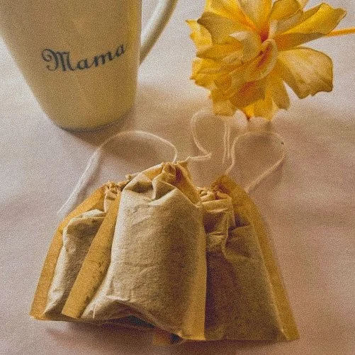 A beige mug with the word 'Mama' on it, a yellow flower in a small vase, and a brown paper bag on a light-colored surface.