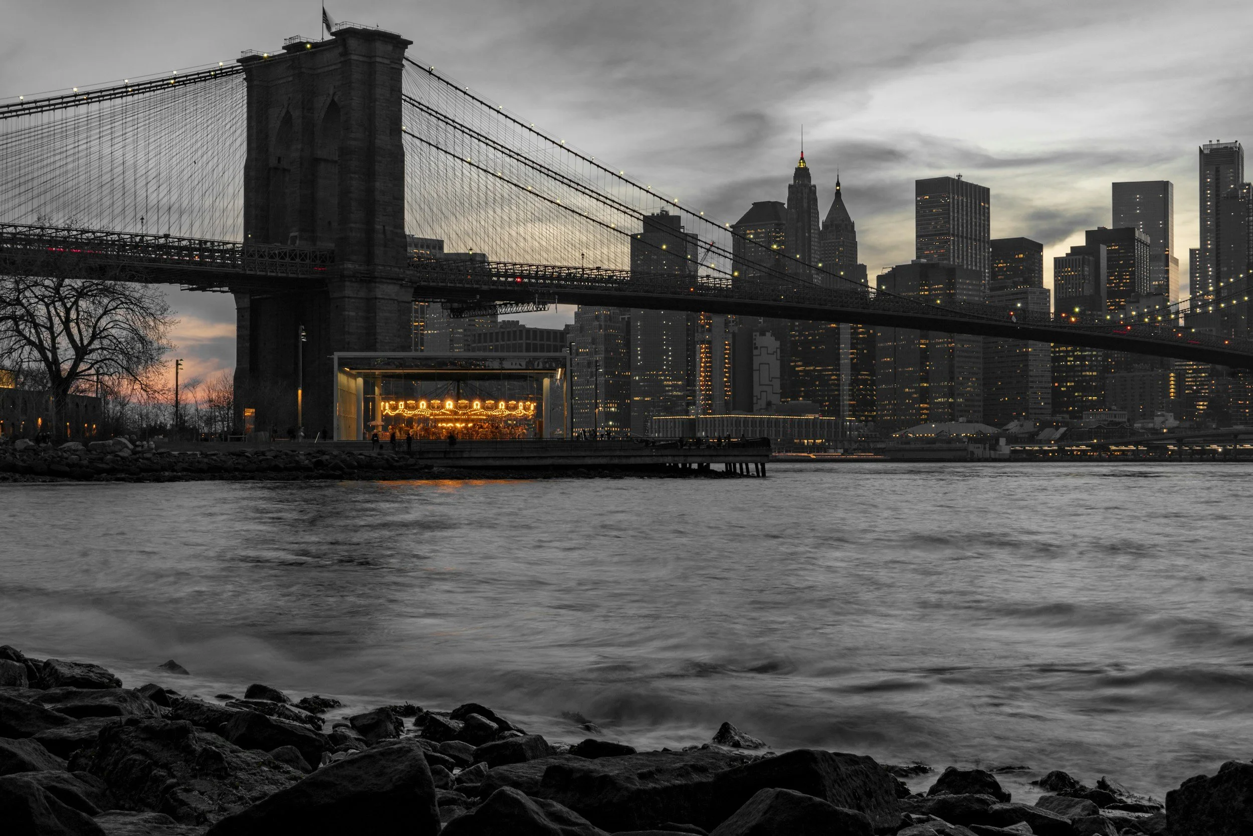 Image of a Jane's Carousel set in the midst of the Hudson River with the Brooklyn Bridge and NYC skyline as the background, in DUMBO,