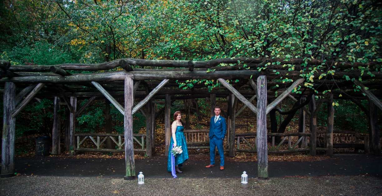 A couple dressed in green standing beneath Prospect Park's Rustic Arbor  after their custom wedding officiated by fun Brooklyn wedding officiant
