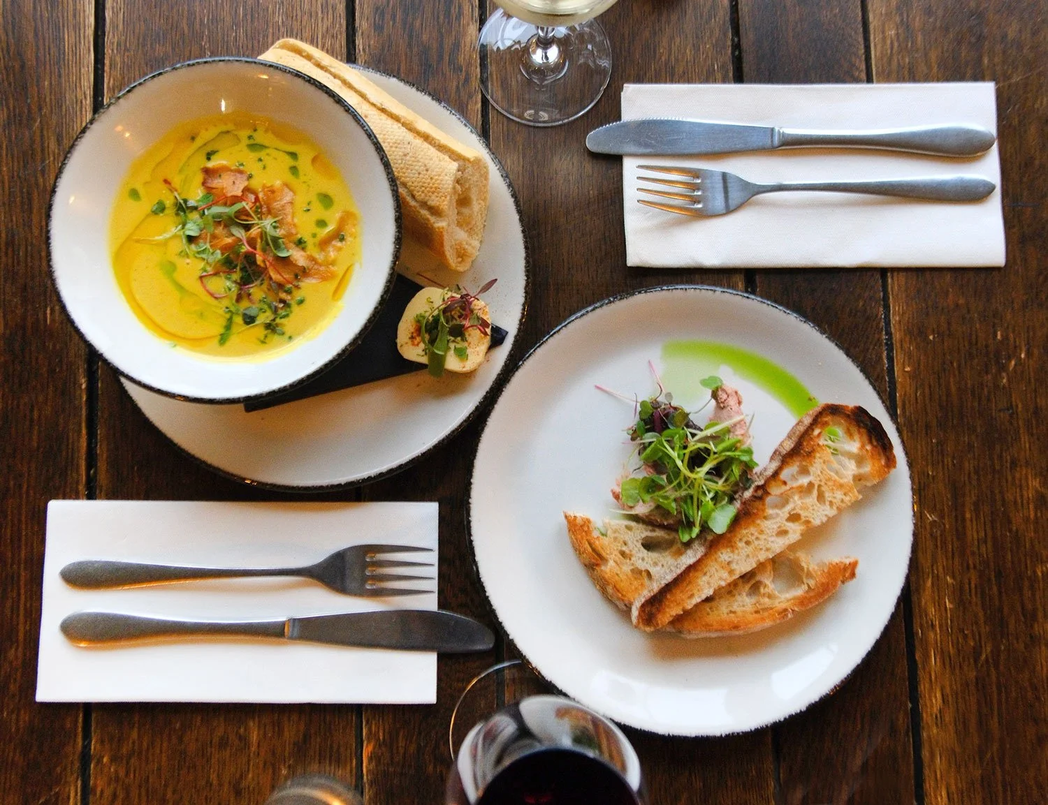 Two glasses of beer on a wooden table in a lively pub, with people socializing in the background.