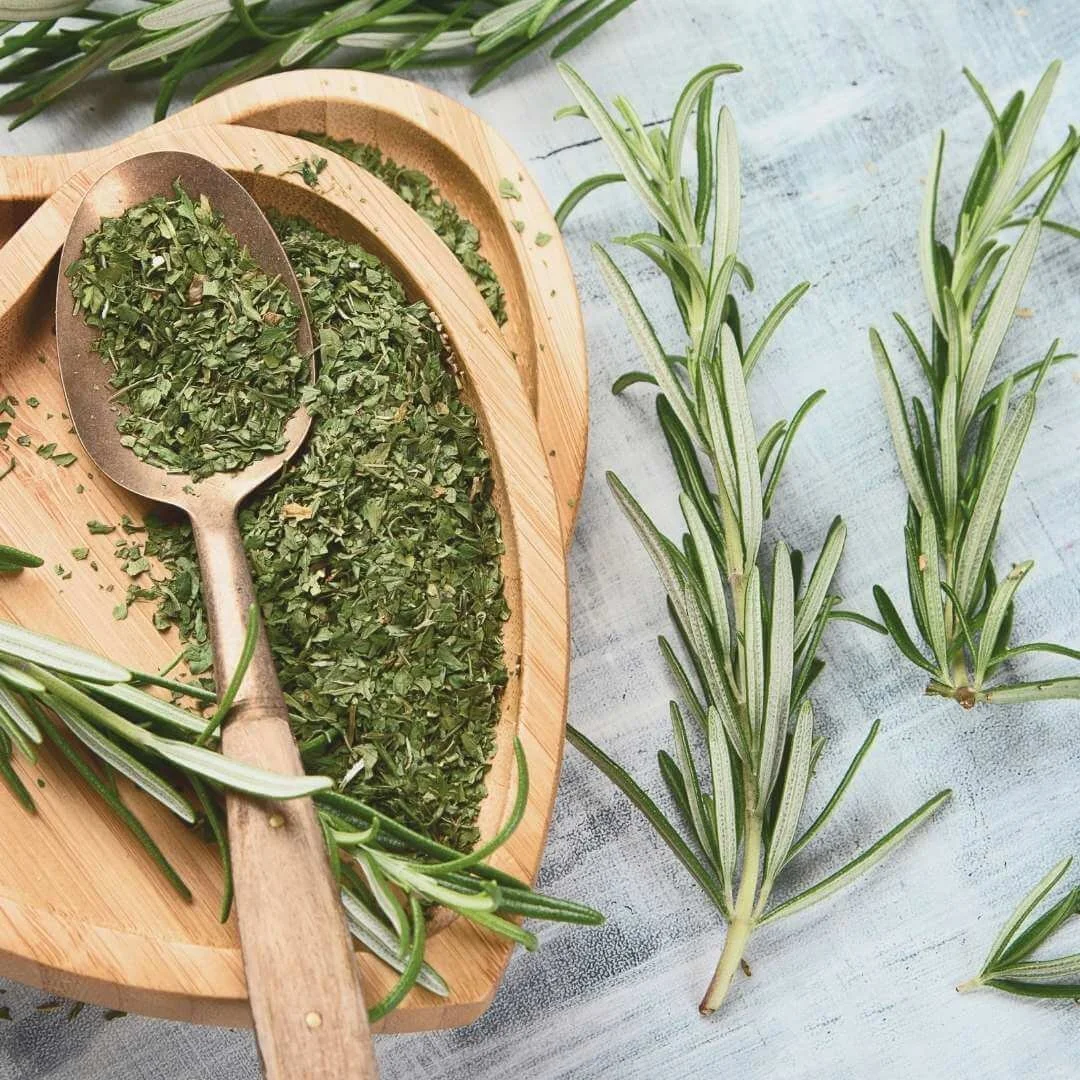 Finely chopped rosemary in a wooden bowl with a spoon and fresh rosemary sprigs beside it.