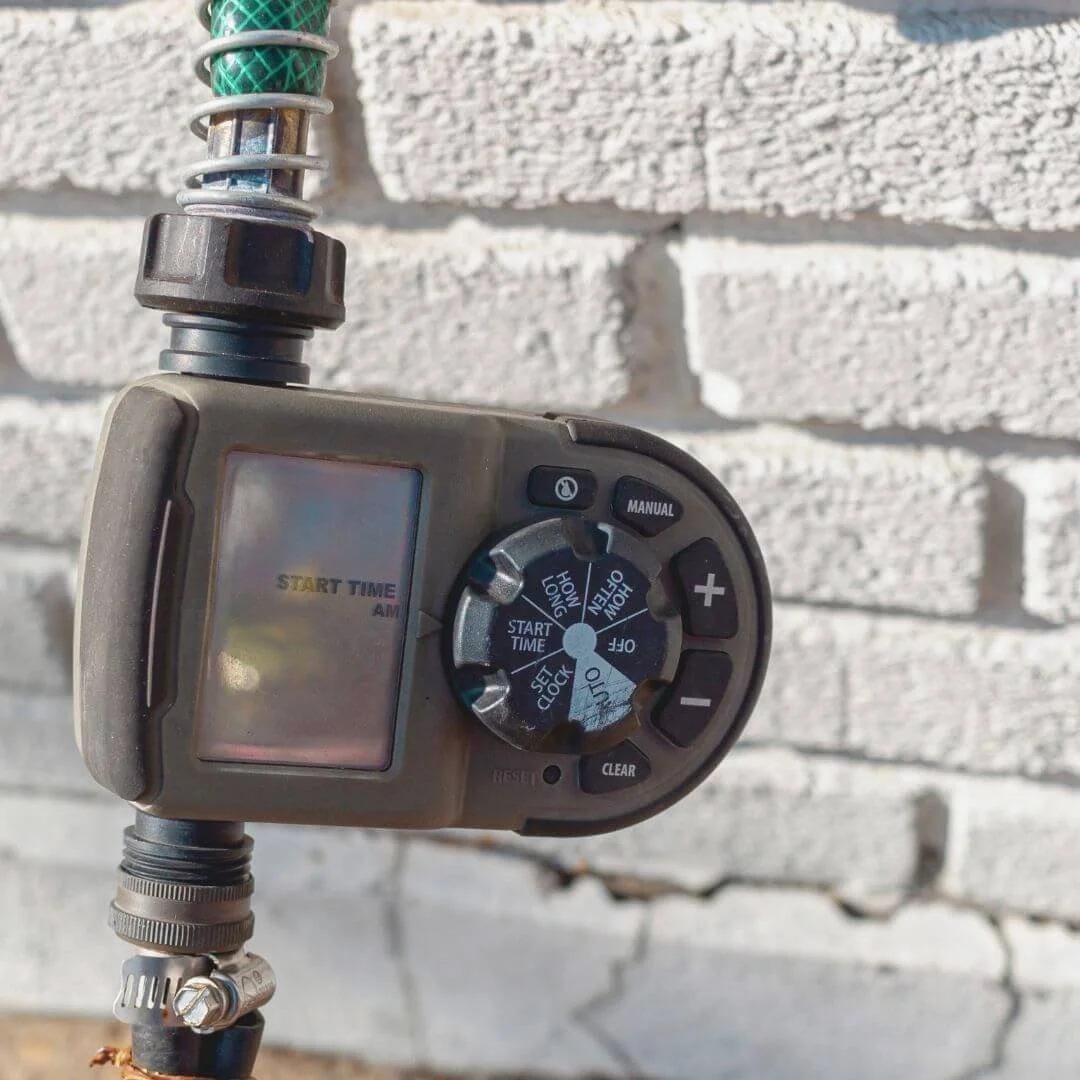 Hose timer connected to an outdoor spigot in front of a white brick wall