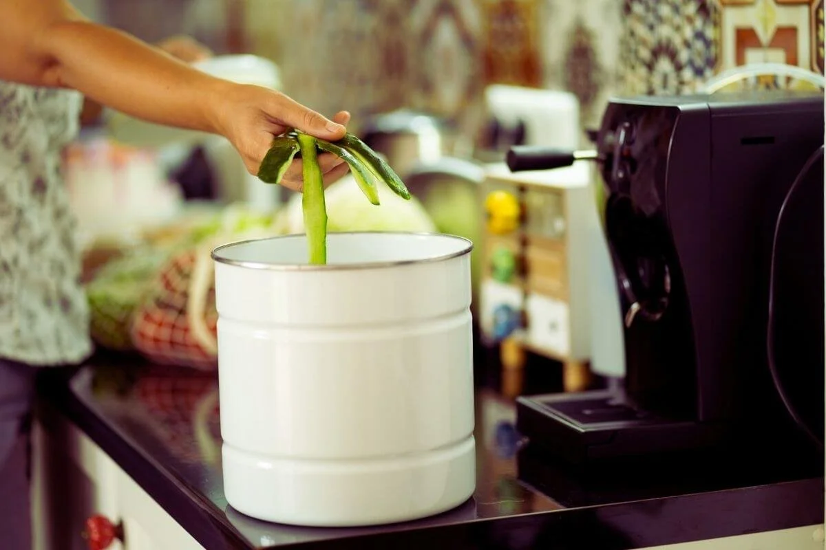 Woman placing vegetable scraps into a countertop kitchen compost bin with charcoal filter