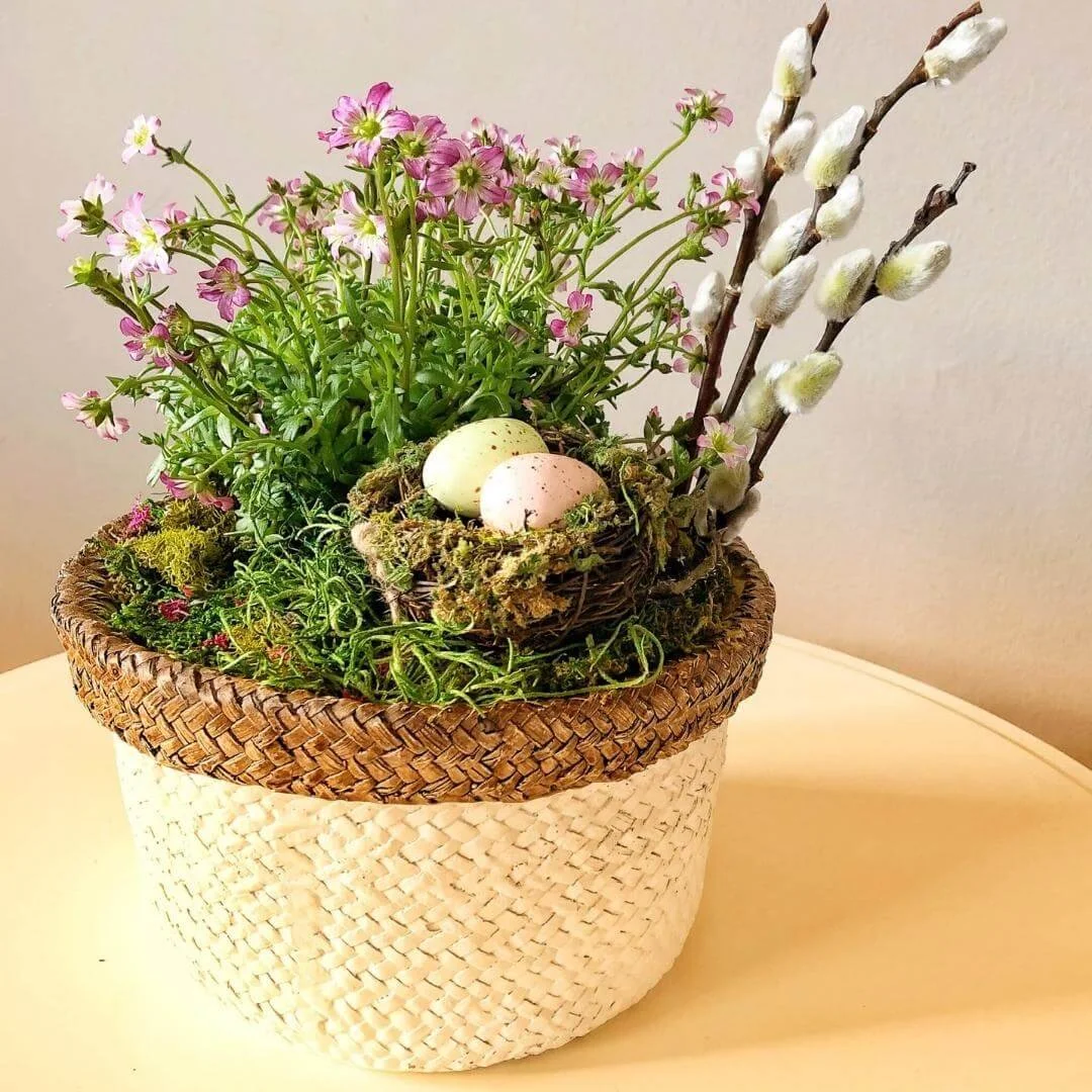 spring tabletop decor arrangement with pussy willows, flowers, easter decorations on white tabletop with white interior wall background