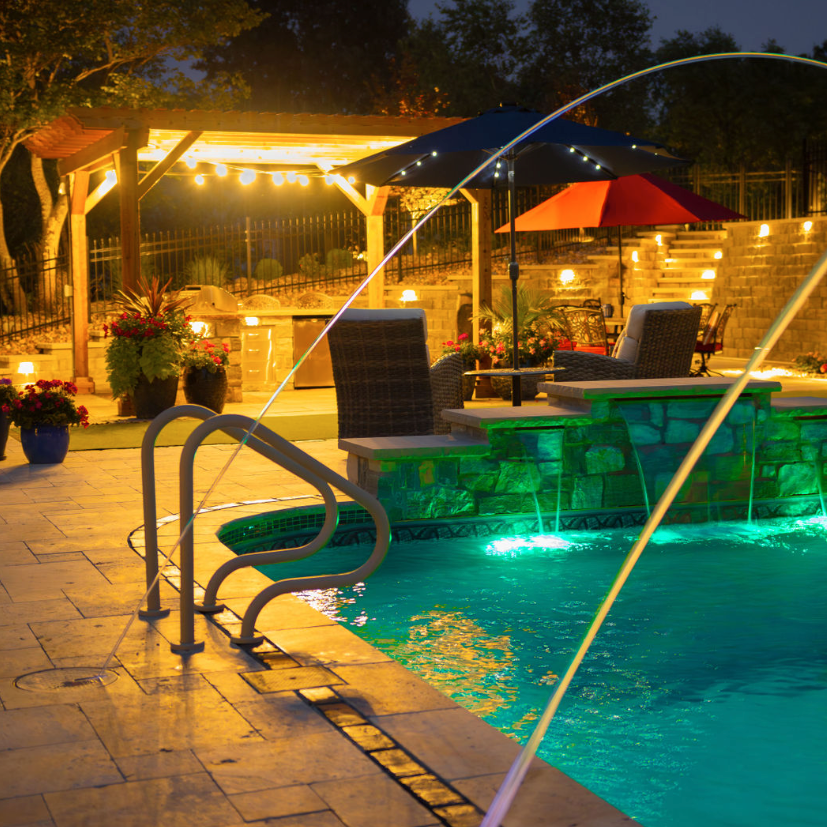 A backyard hardscape in Kansas City that was a pool, paver patio, and pergola that is well lit by lighting at night