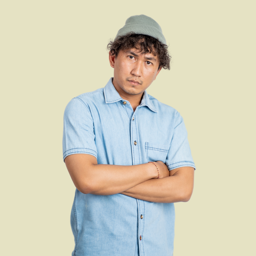 [Image] Hispanic young adult with crossed arms in blue shirt and green hat, seeming stressed and upset. Denver Teen Stress Managment Therapy.