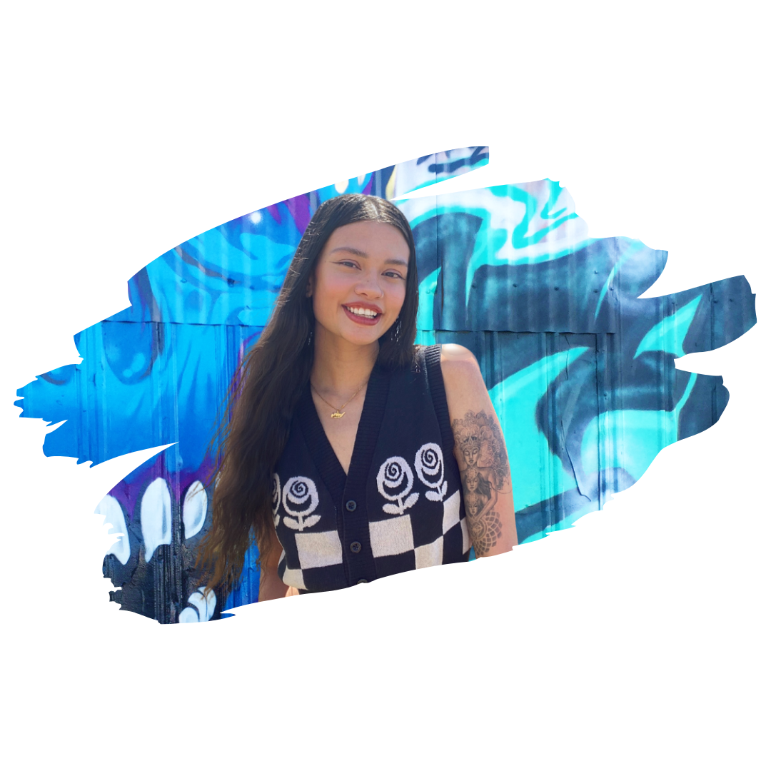 [Image] AAPI non-binary person standing with hands at side, smiling in front of a graffiti wall mural; Rani Ellison Asian Teen and Young Adult Therapist at Interfaith Bridge Counseling in Denver, CO.