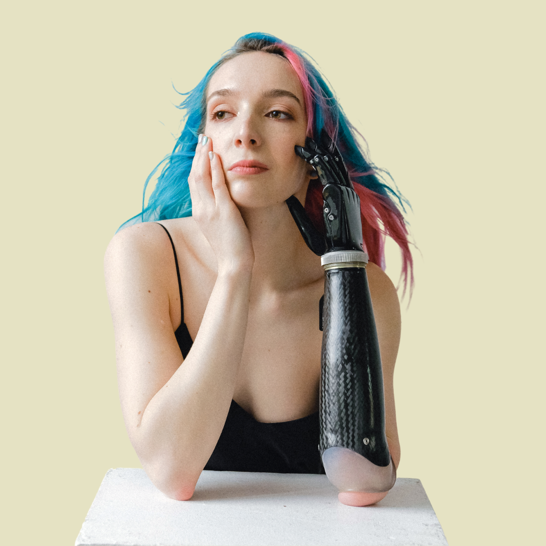 [Image] Caucasian young adult with prosthetic arm holding chin and blue and pink hair. Denver Young Adult Therapy for Stress.