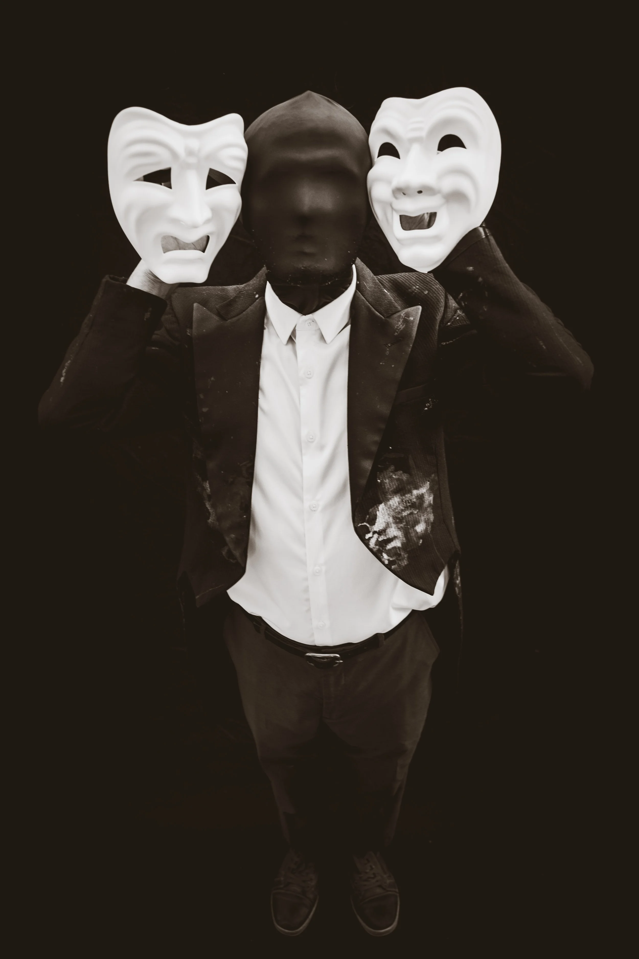 Faceless man holds two drama masks on either side of face.