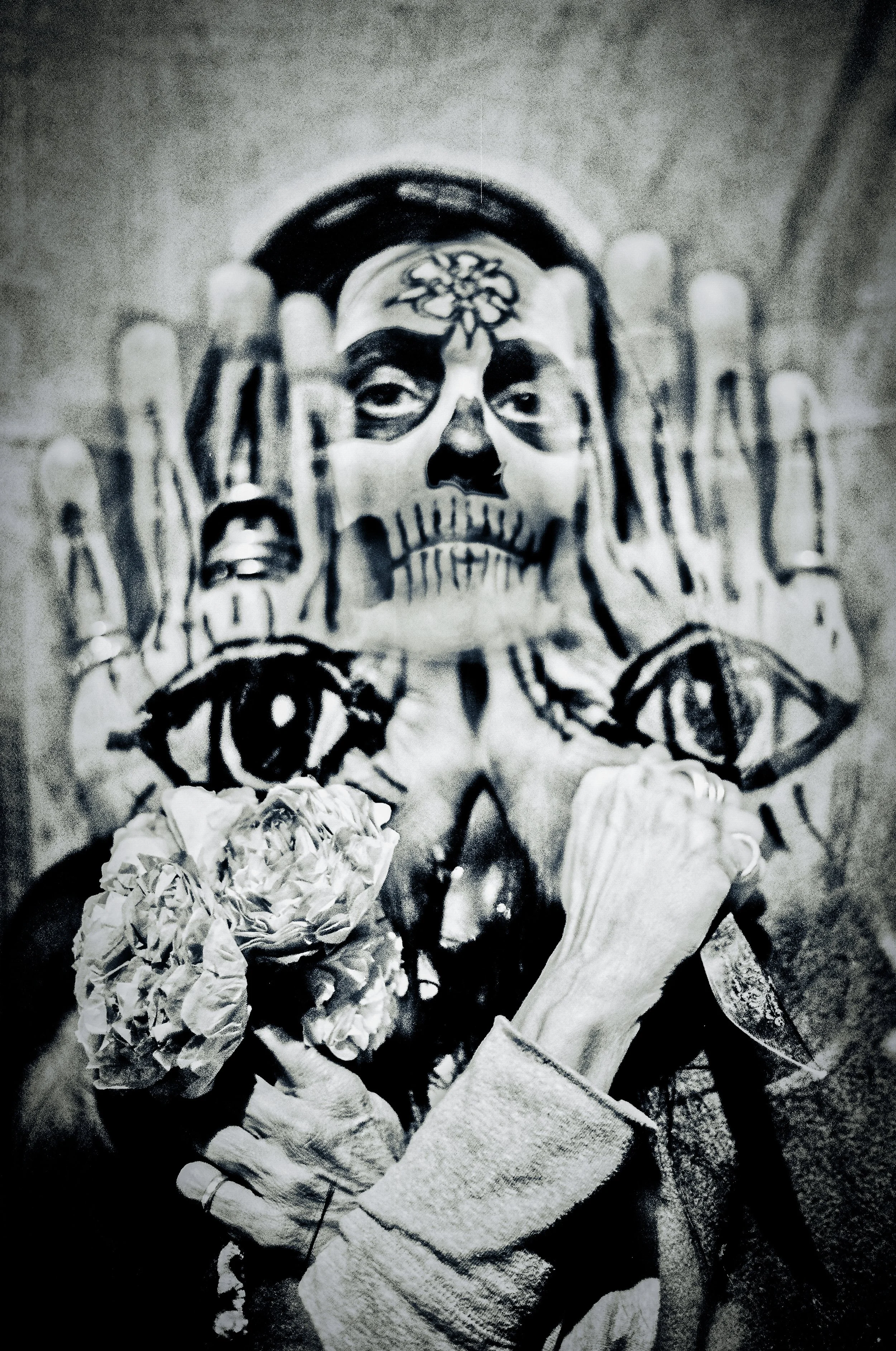 Multiple exposure black and white image of a woman in dio de los muertos makeup, holding her hands up that are painted with eyes