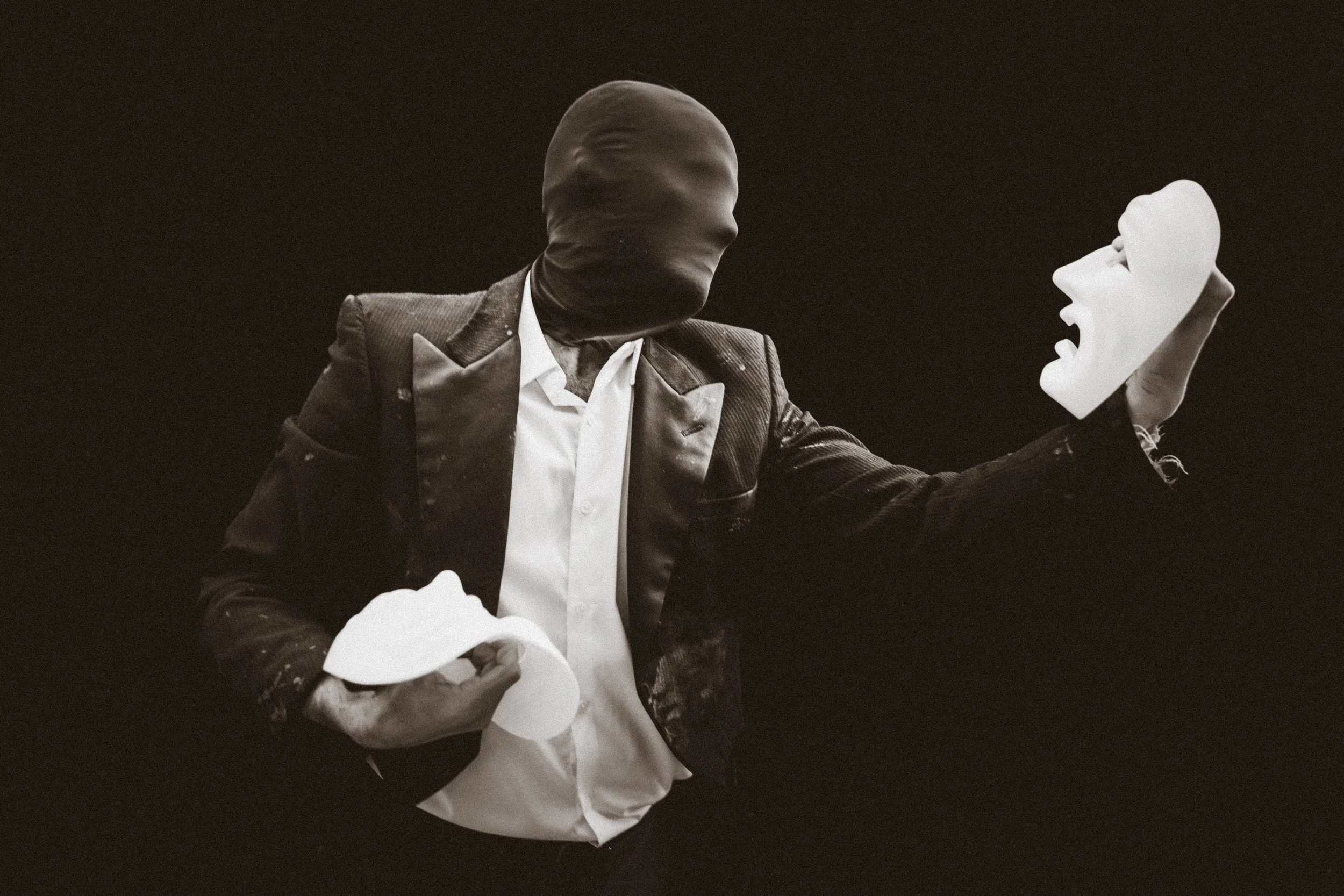 Faceless man holds two white masks, debates which to choose.