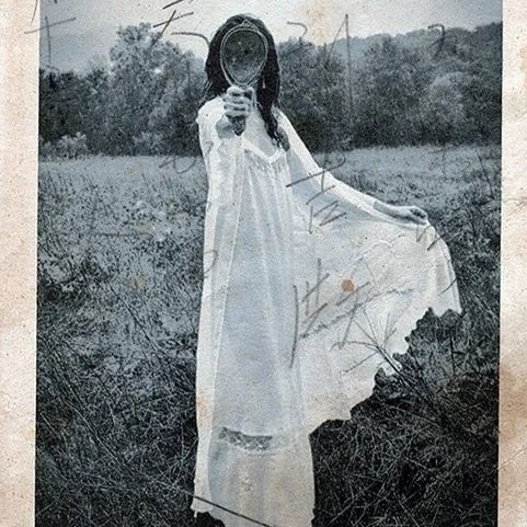 Black and white image of a woman in a white night gown holding up a hand mirror that completely obscures her face to the camera, printed over a vintage japanese postcard