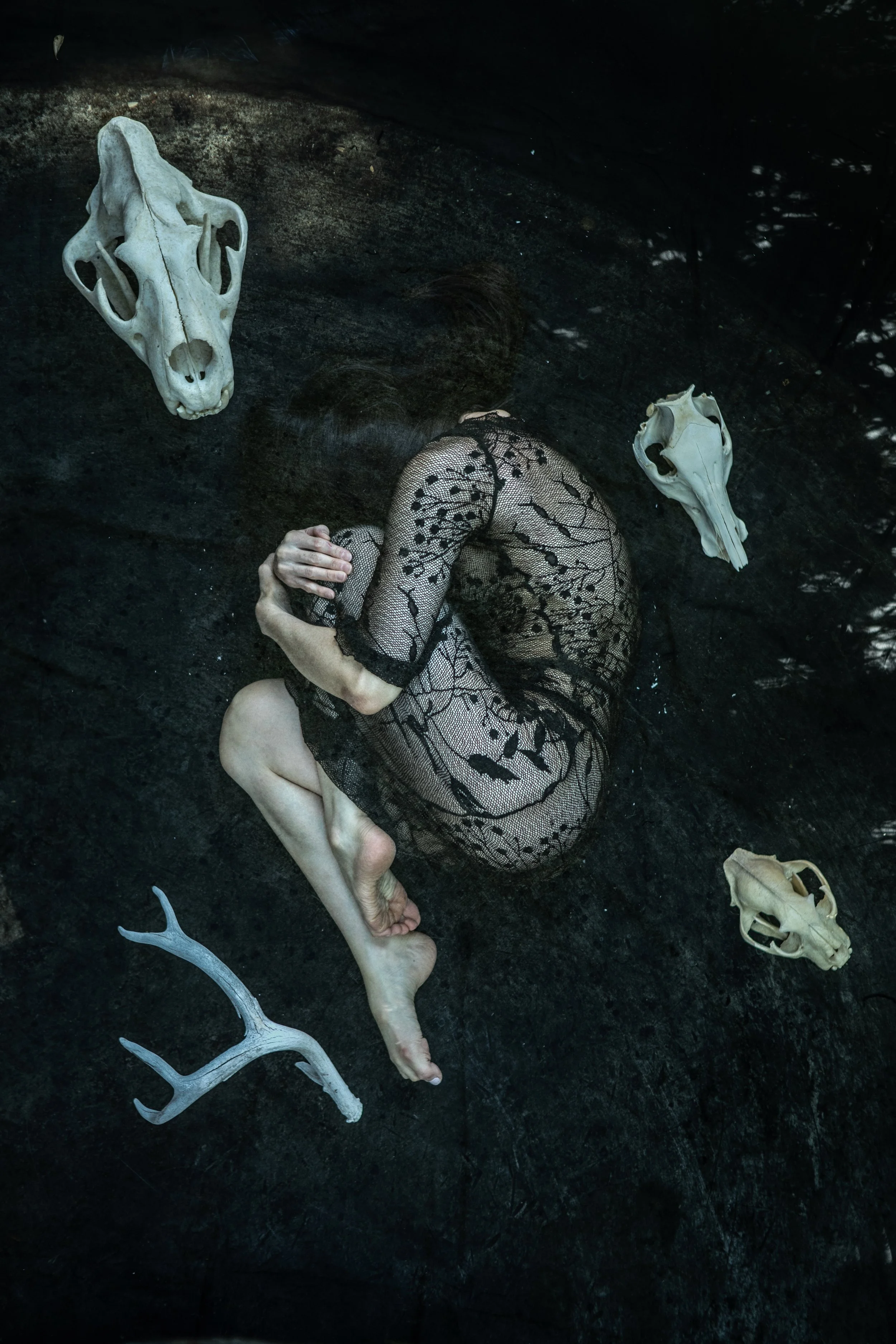 Woman curled in fetal position with animal skulls around her