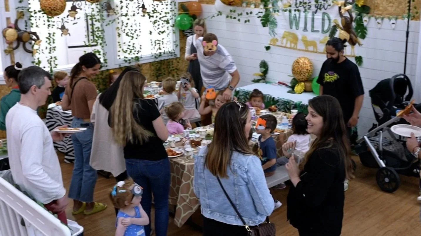 Children and adults celebrating a wild animal-themed birthday party with jungle decorations, balloons, and games.