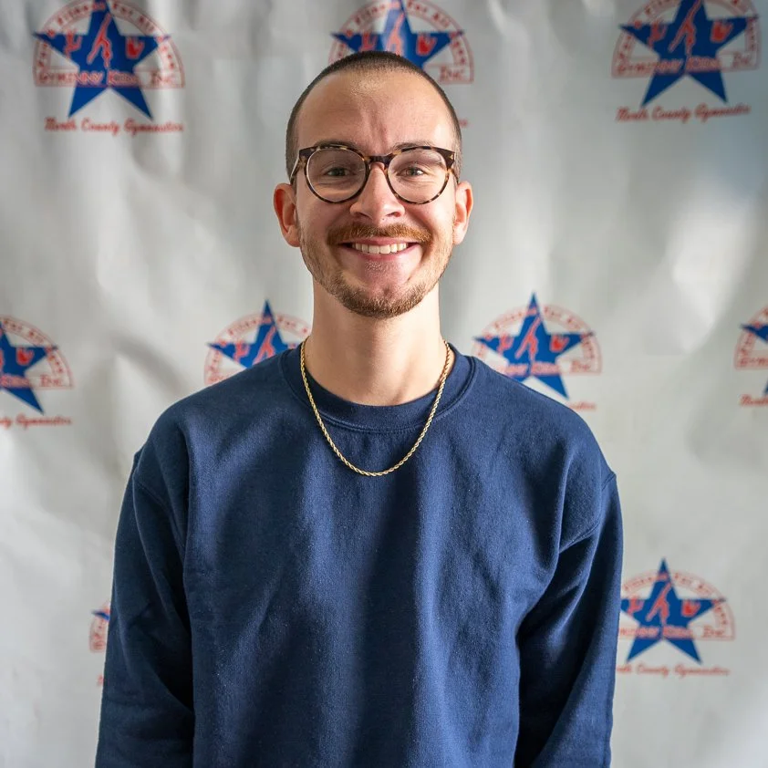 A smiling man with glasses and a gold chain posing in front of a backdrop with the Texas County GOP logo.