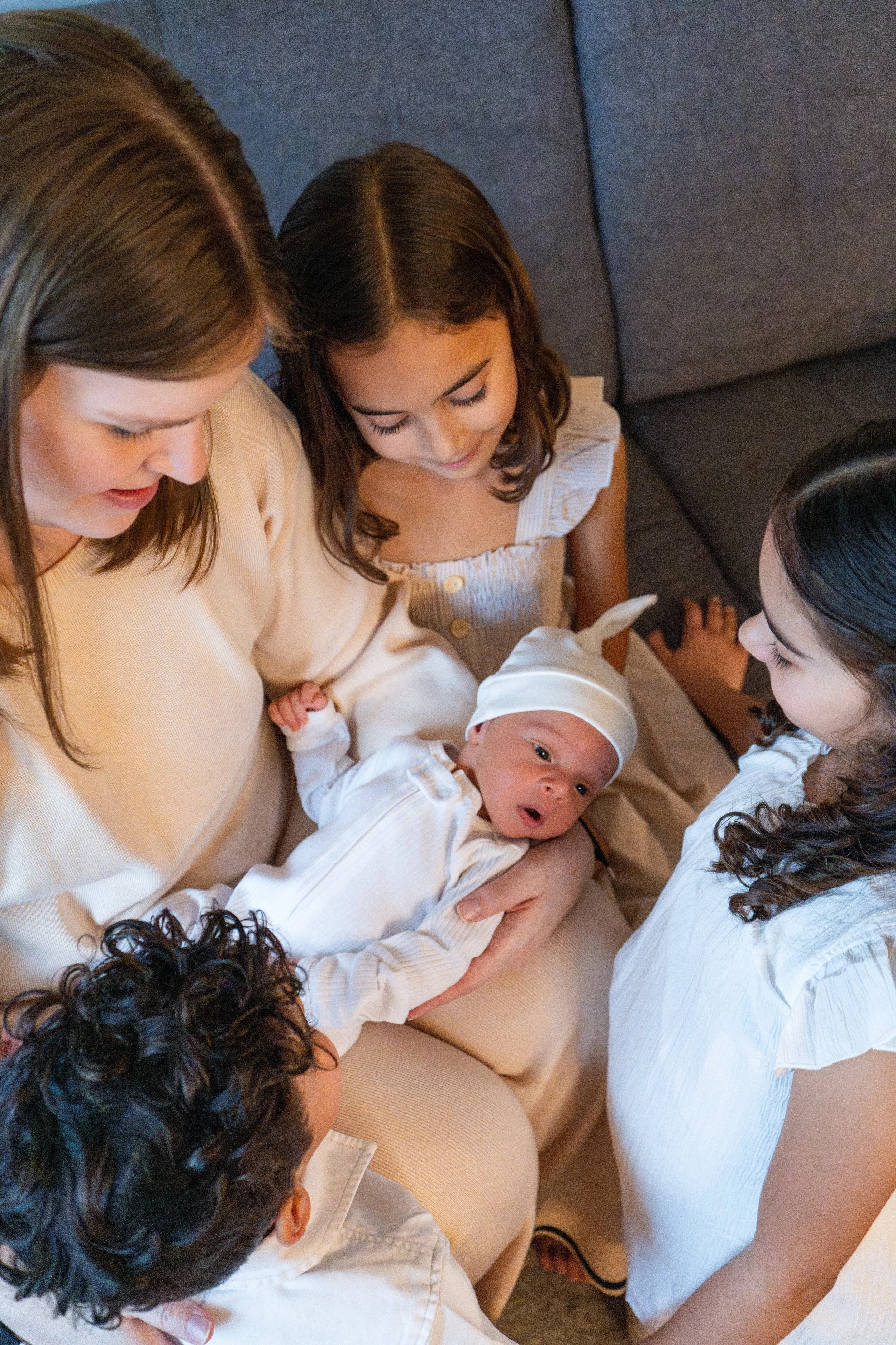 A woman holding an infant and surrounded by children, sitting on a couch