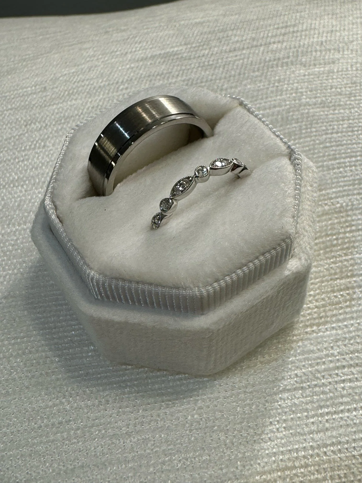 A white jewelry box with a wedding band and a diamond ring inside.
