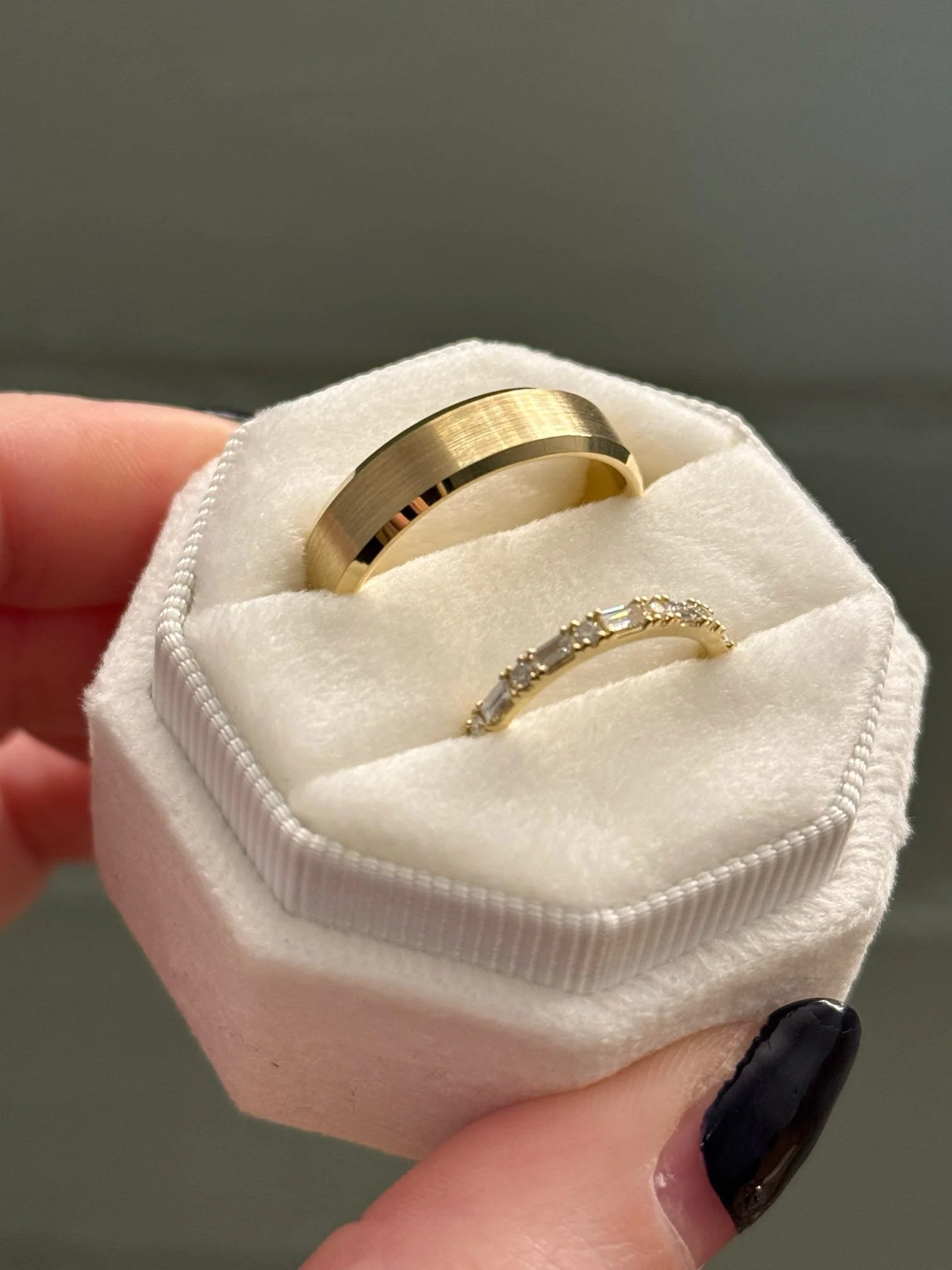 A white velvet ring box containing a gold wedding band and a diamond engagement ring.