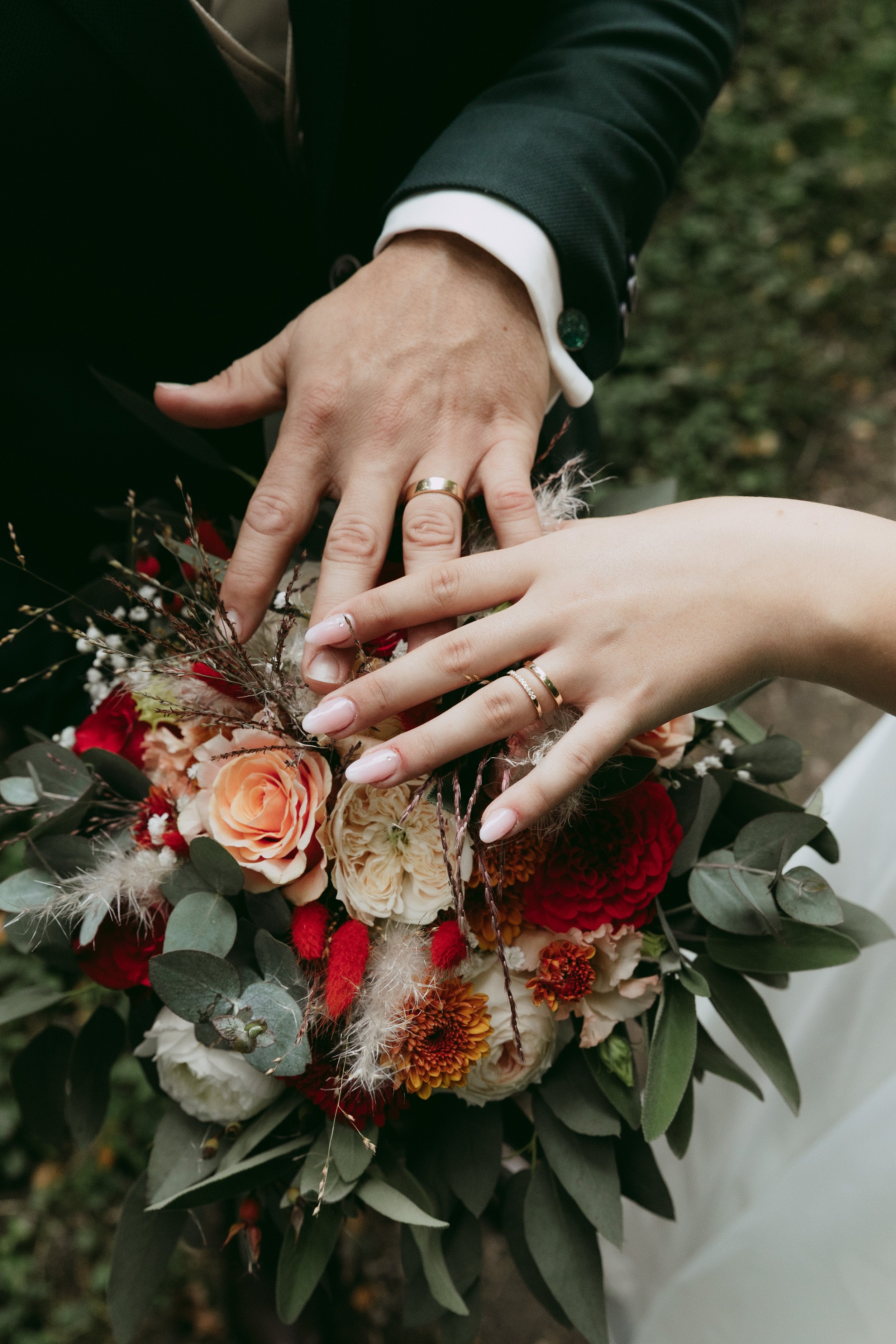 Close-up of a couple's hands showing wedding rings, resting on a bouquet of flowers, on their wedding day.
