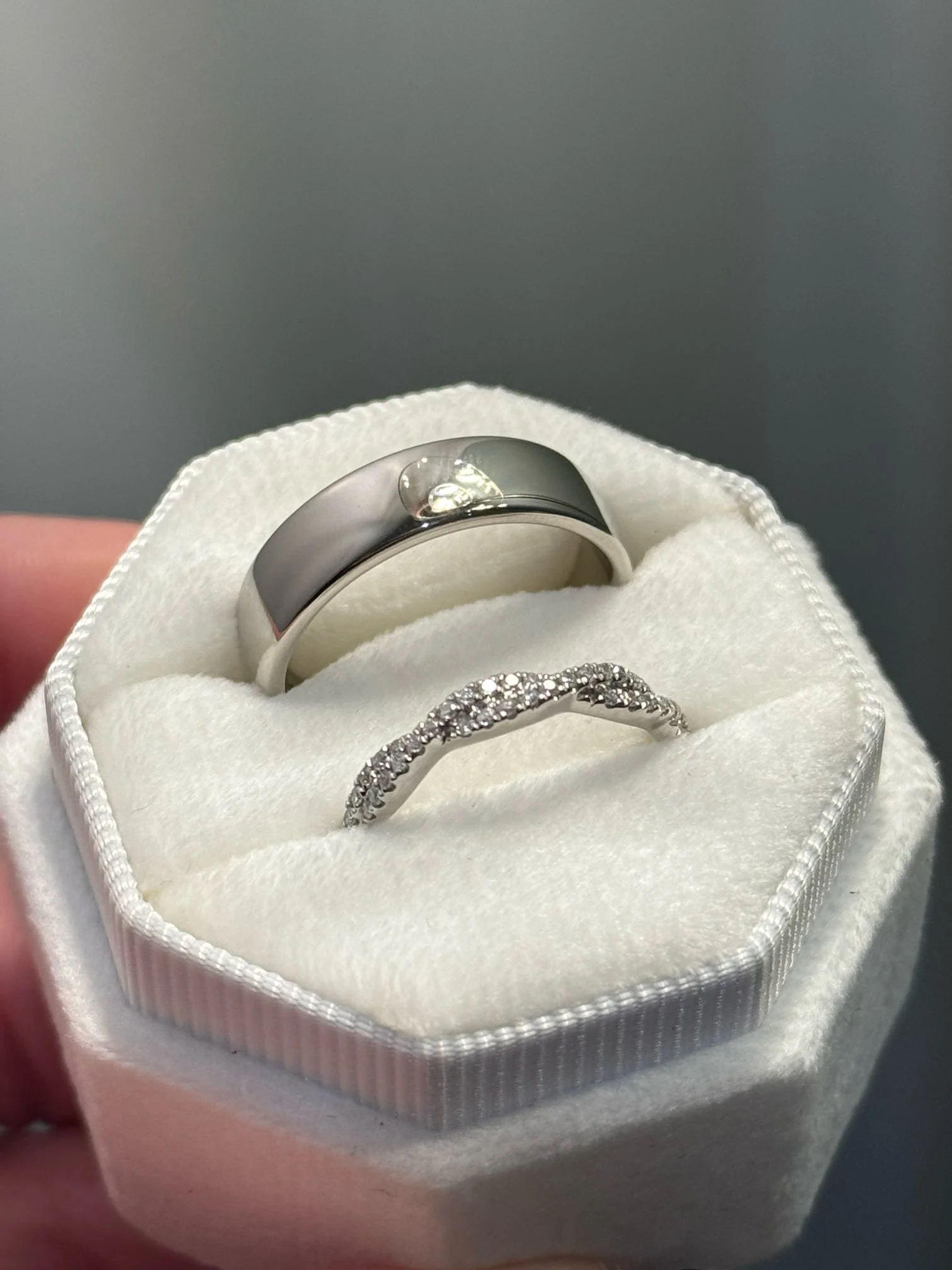 Two silver rings with one encrusted with small diamonds, in a white ring box with pink outside and white interior.